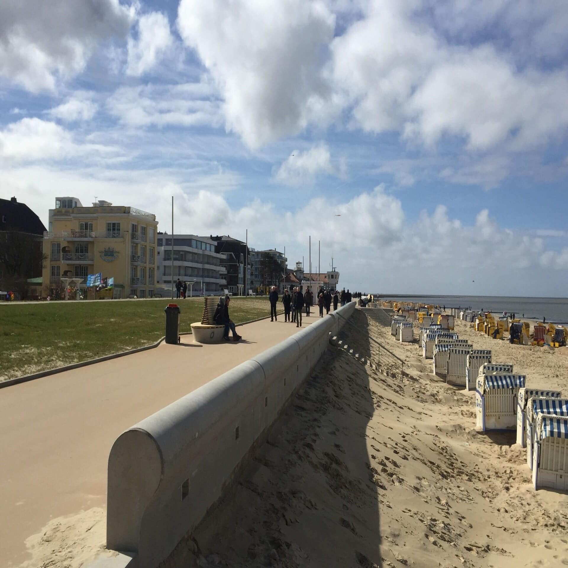 Spaziergänger an der Strandpromenade, rechts Strandkörbe, Links Gebäude.