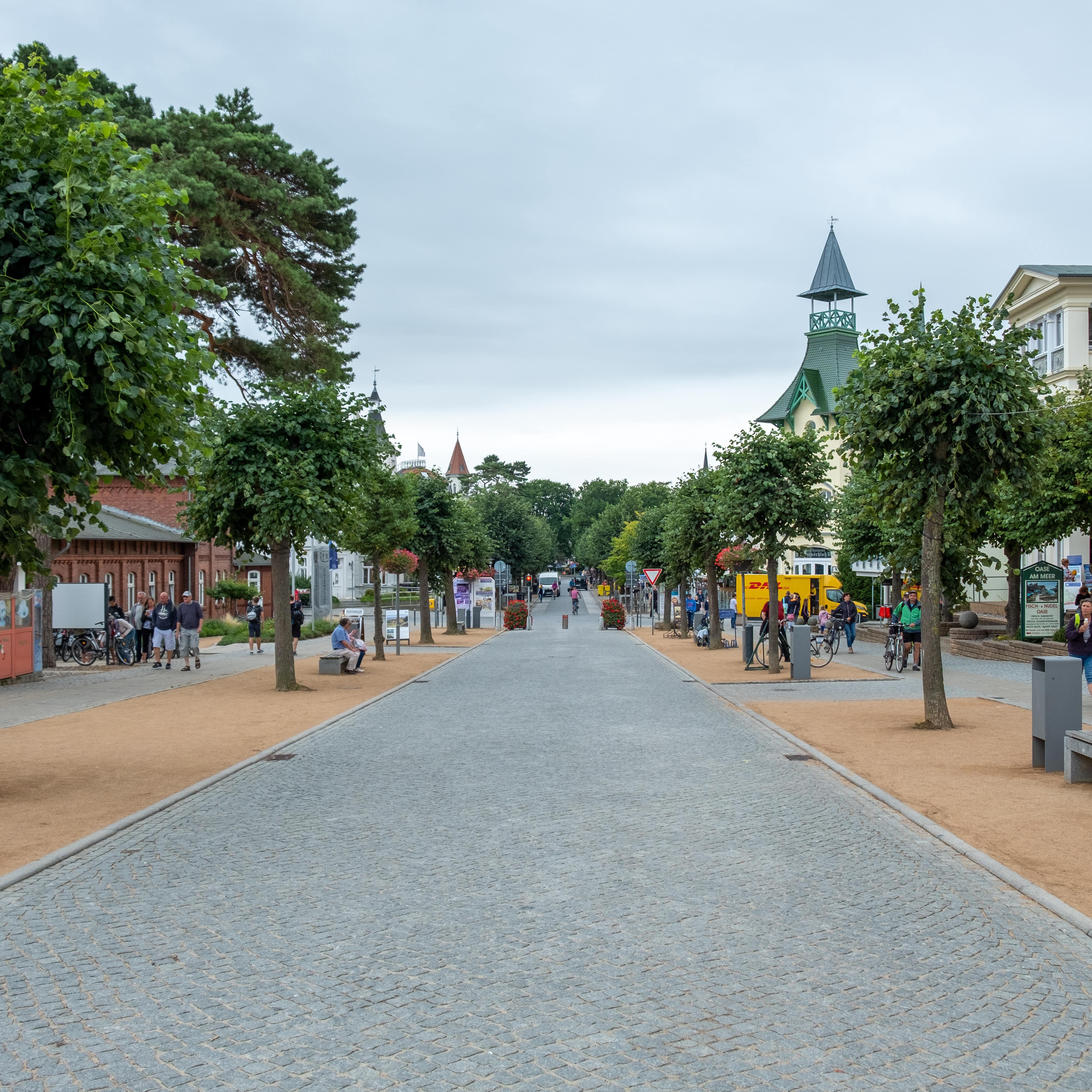 Eine Straße in Zinnowitz, links und rechts Bänke, Bäume und Leute.
