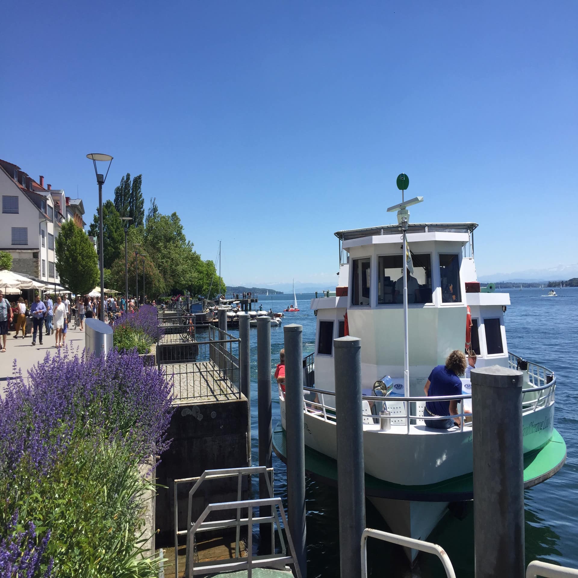 Blick entlang der sonnigen Promenade in Überlingen, rechts Bootsanleger und ein Boot.