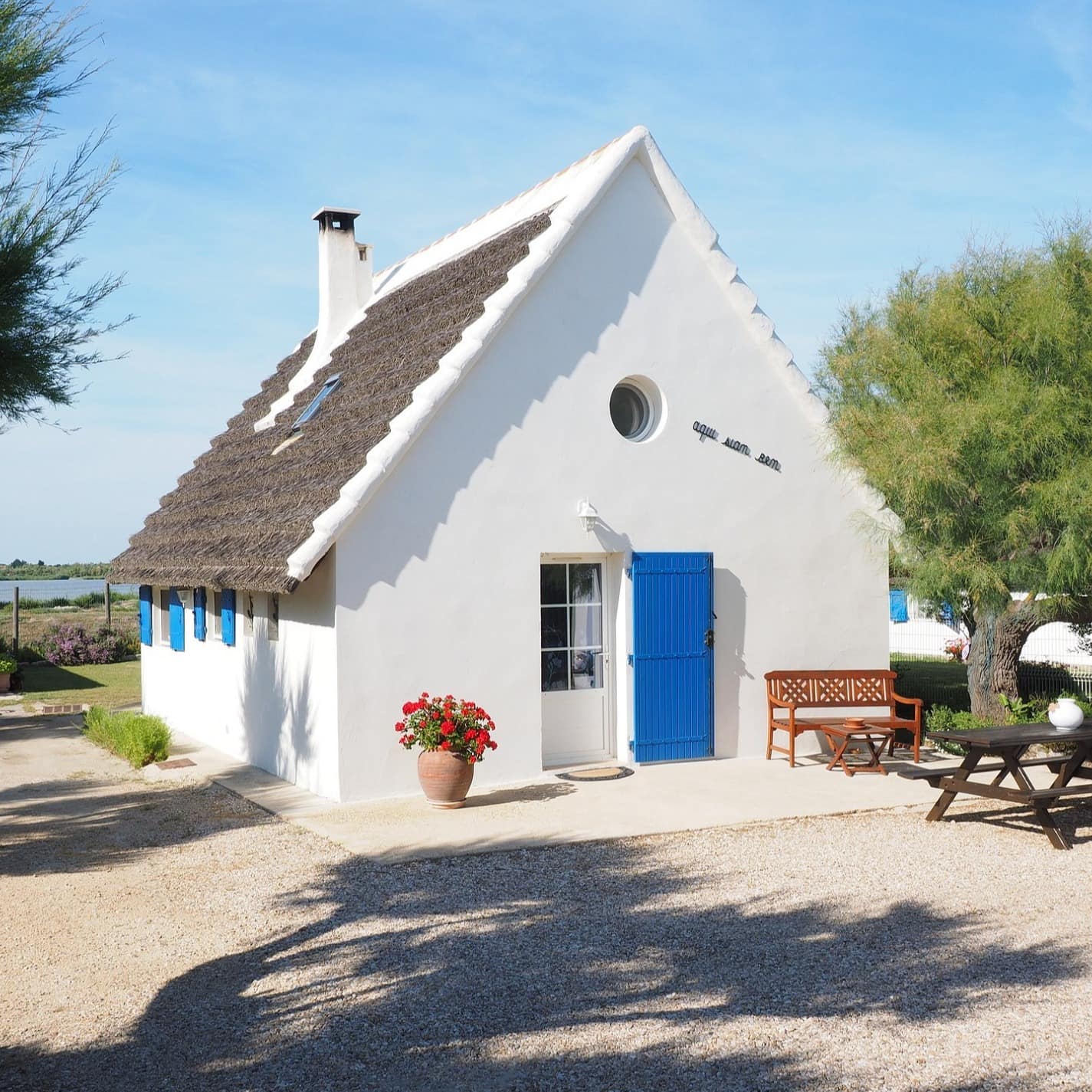 Ein eher moderneres Ferienhaus in Frankreich mit blauer Tür, und roten Blumen sowie Sitzgelegenheiten auf der Terrasse