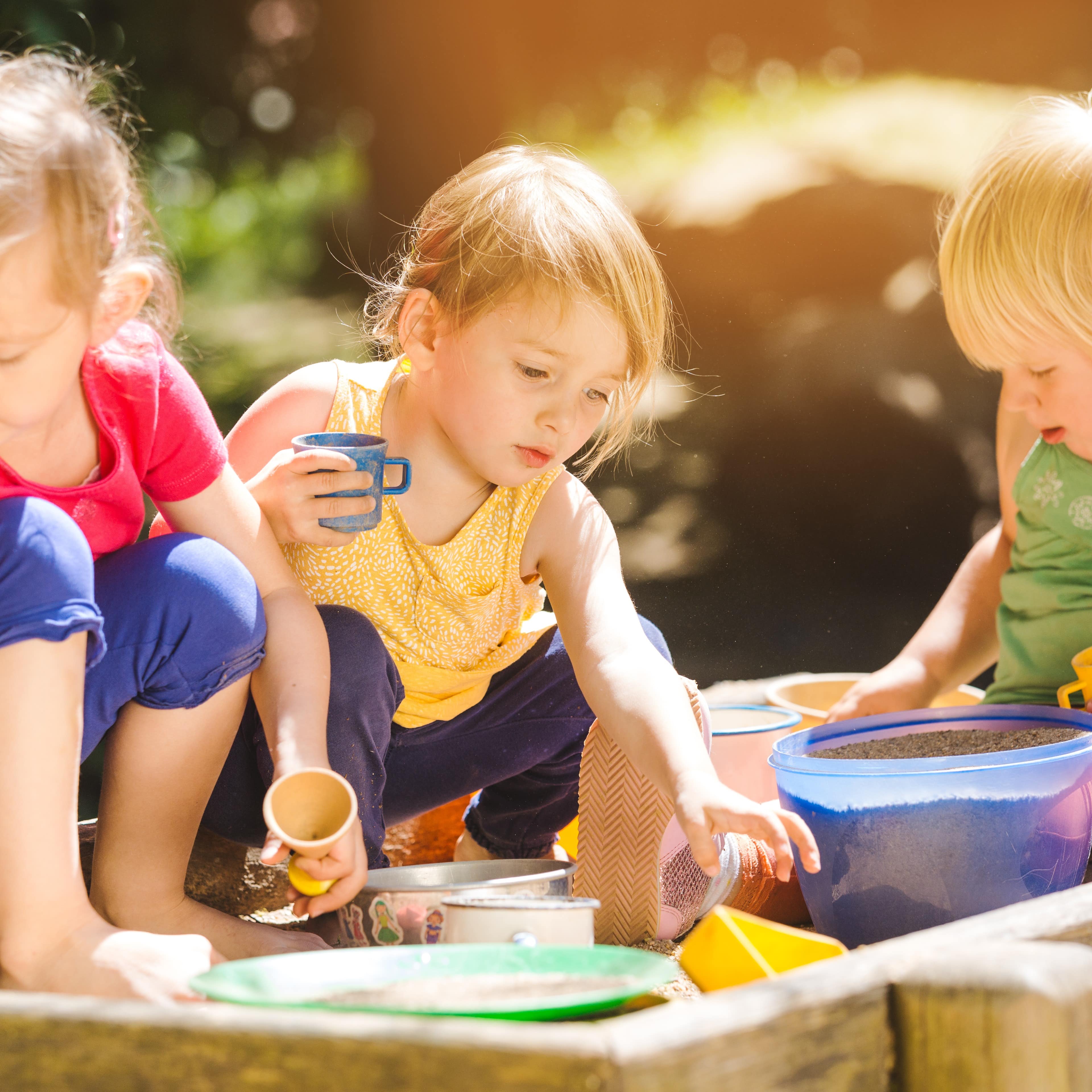 3 kleine Mädchen spielen in einer Sandkiste.