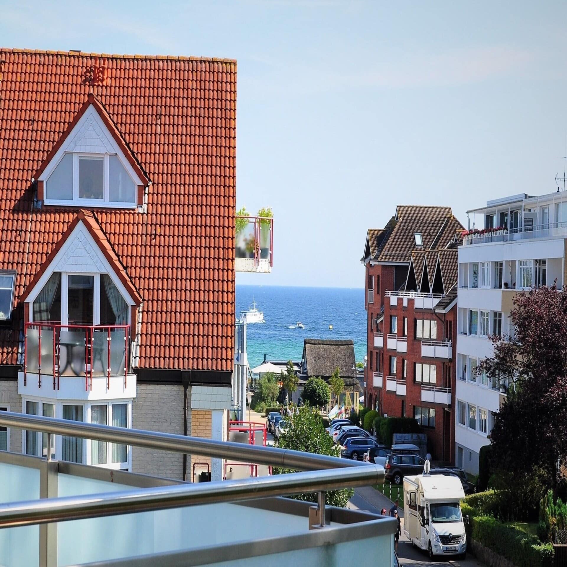 Blick von einem Balkon auf Häuser und eine Straße, die auf die Ostsee zuführt. 