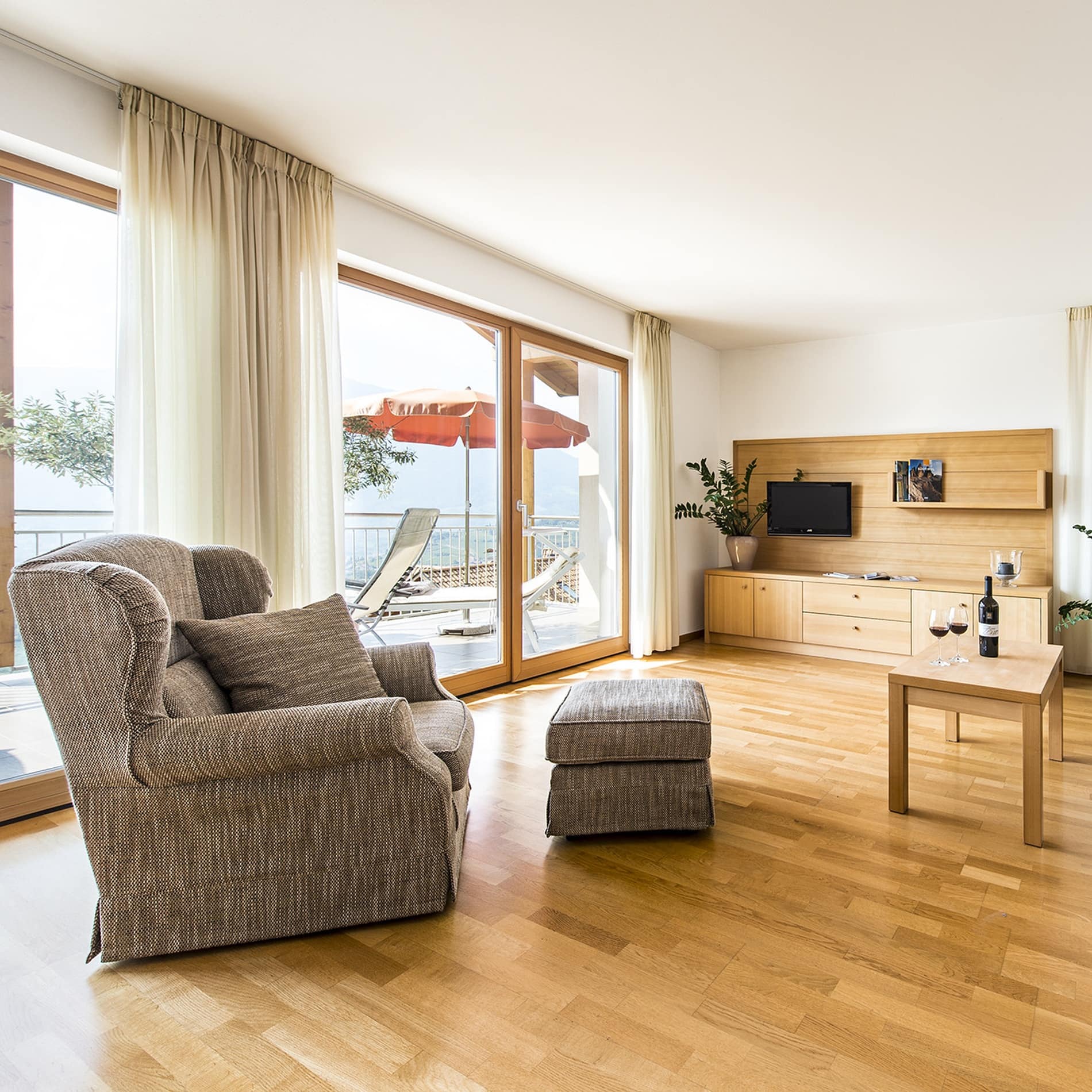 Eine breite Panorama-Fensterfront gibt den Blick vom Wohnzimmer der Ferienwohnung in Schenna frei auf den Balkon und das Meraner Tal