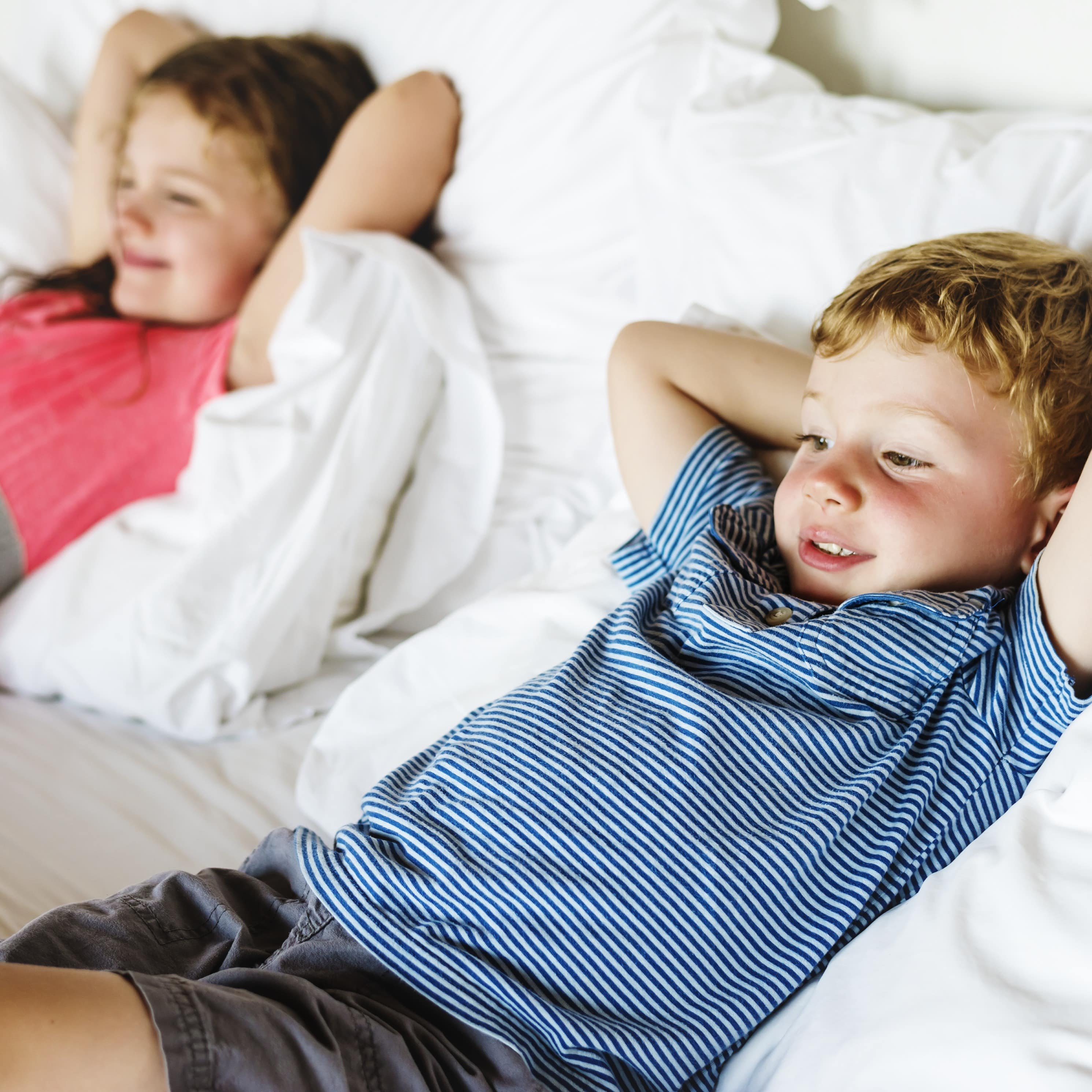 Ein Junge und ein Mädchen liegen mit hinter dem Kopf verschränkten Armen auf einem Bett.