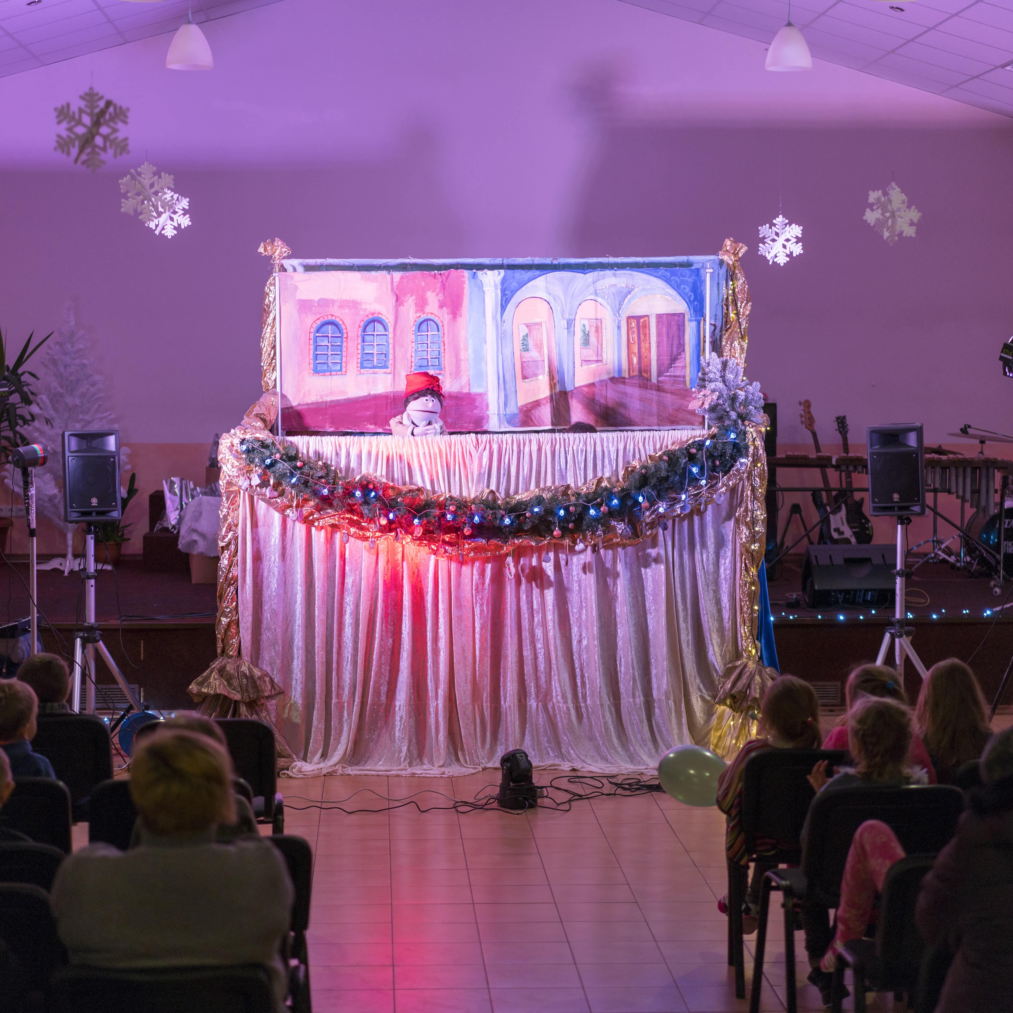 Blick durch einen abgedunkelten Saal in dem Erwachsene und Kinder ein Puppenspiel anschauen.