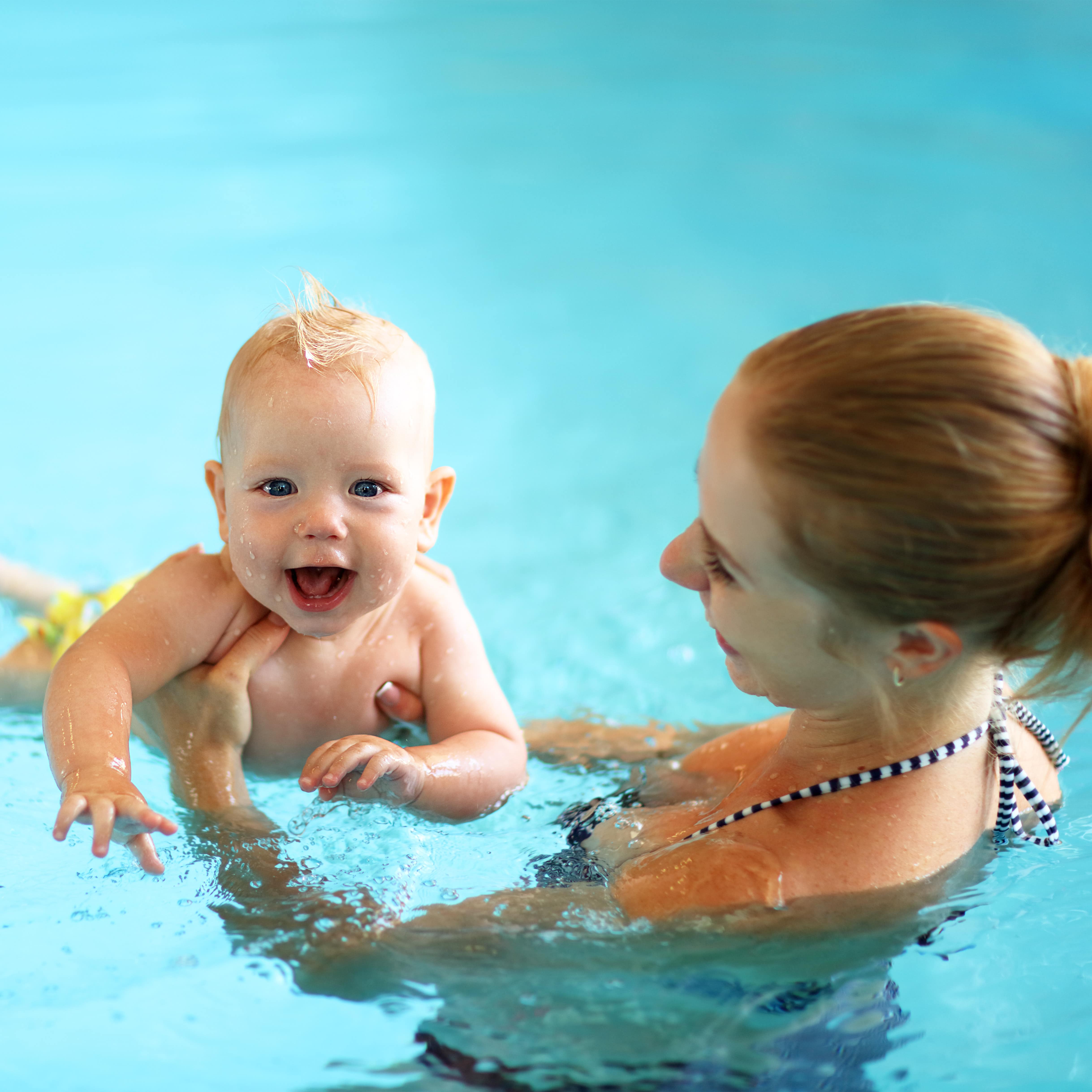 Eine junge Mutter mit ihrem Baby im Pool, das Baby lacht in die Kamera.
