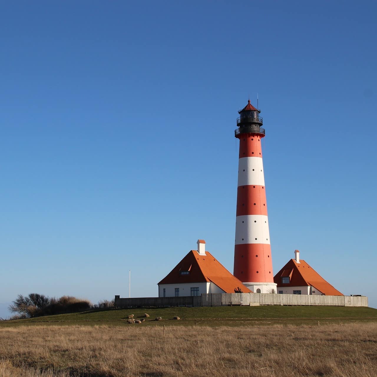 Blick über die Landschaft auf einen Leuchtturm und zwei Häuser in Eiderstedt
