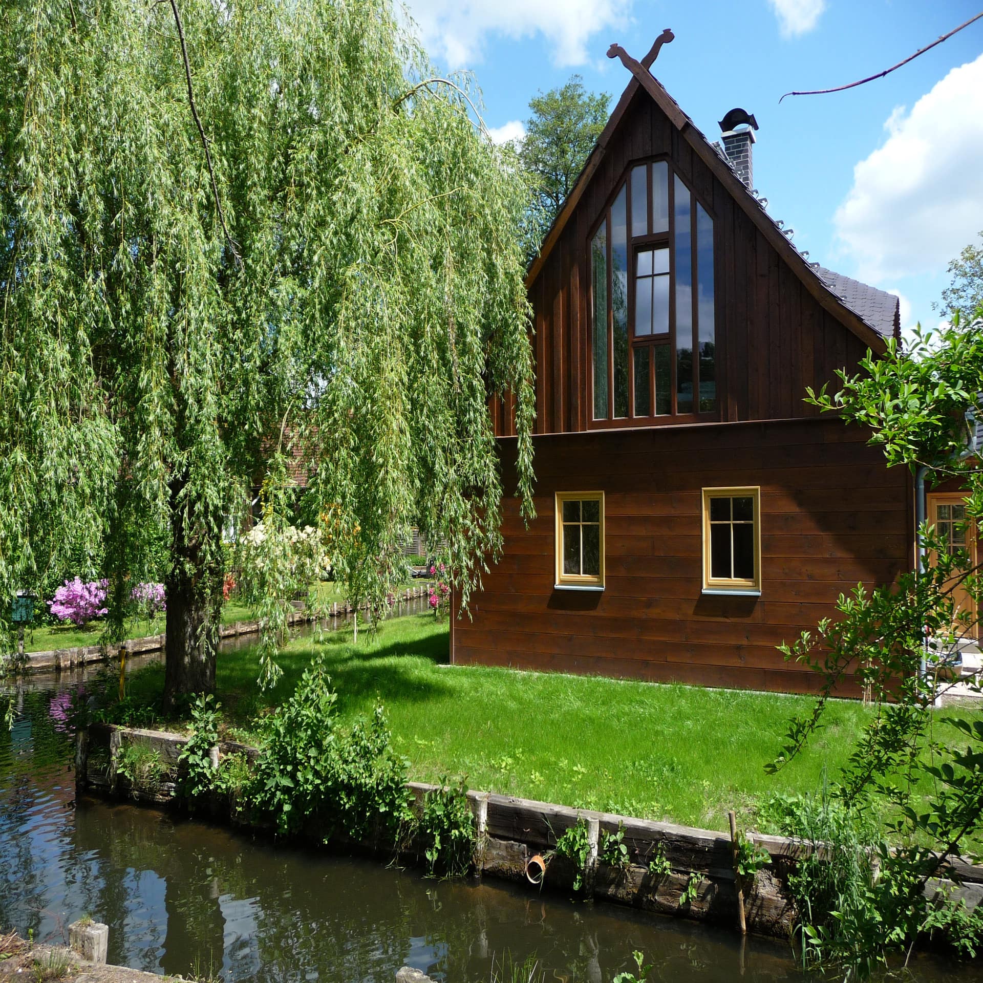Dunkles Holzhaus mit Garten direkt am Wasser im Spreewald.