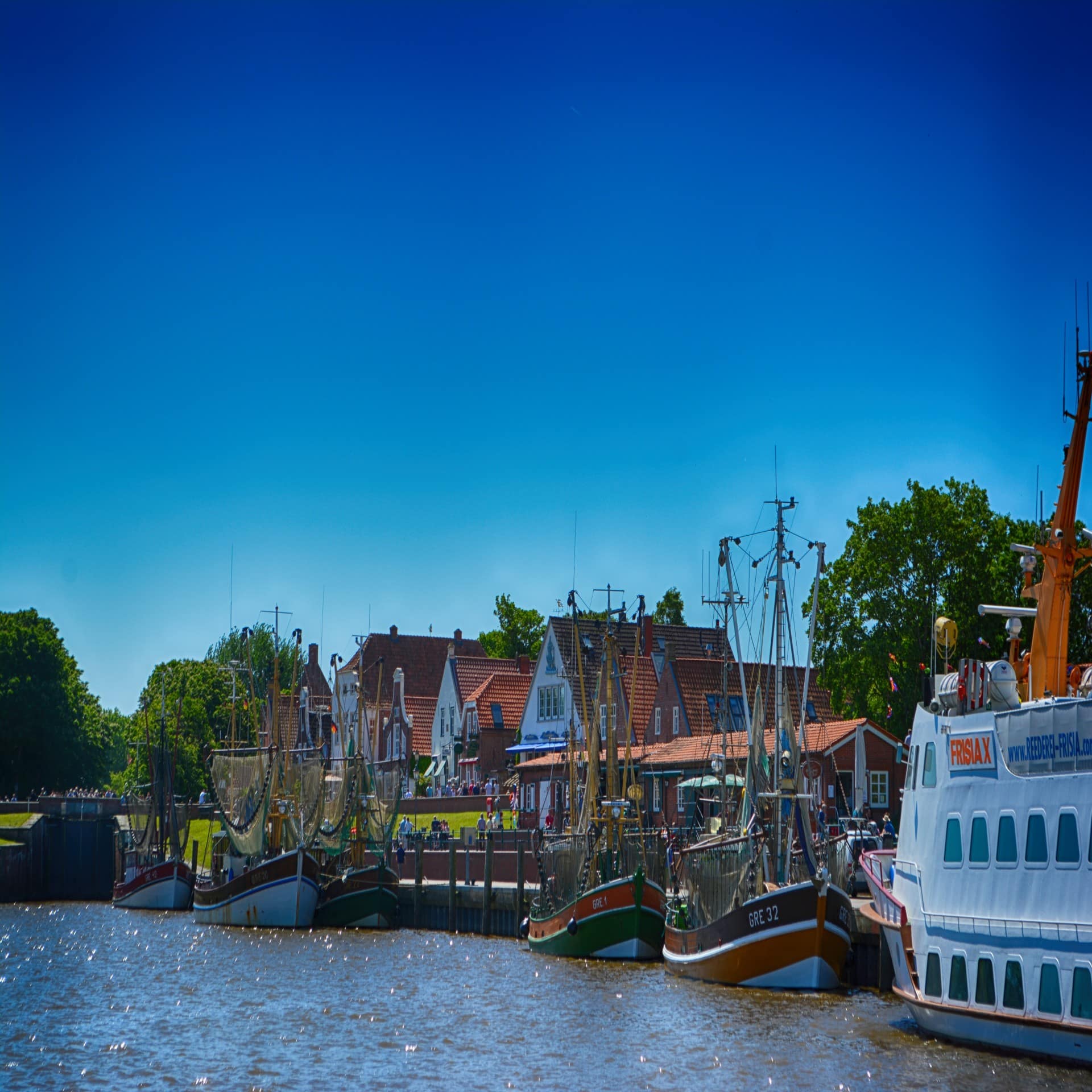 Blick auf den kleinen Hafen von Greetsiel mit Fischerbooten  vor Anker und Häusern im Hintergrund. Sonnenschein.