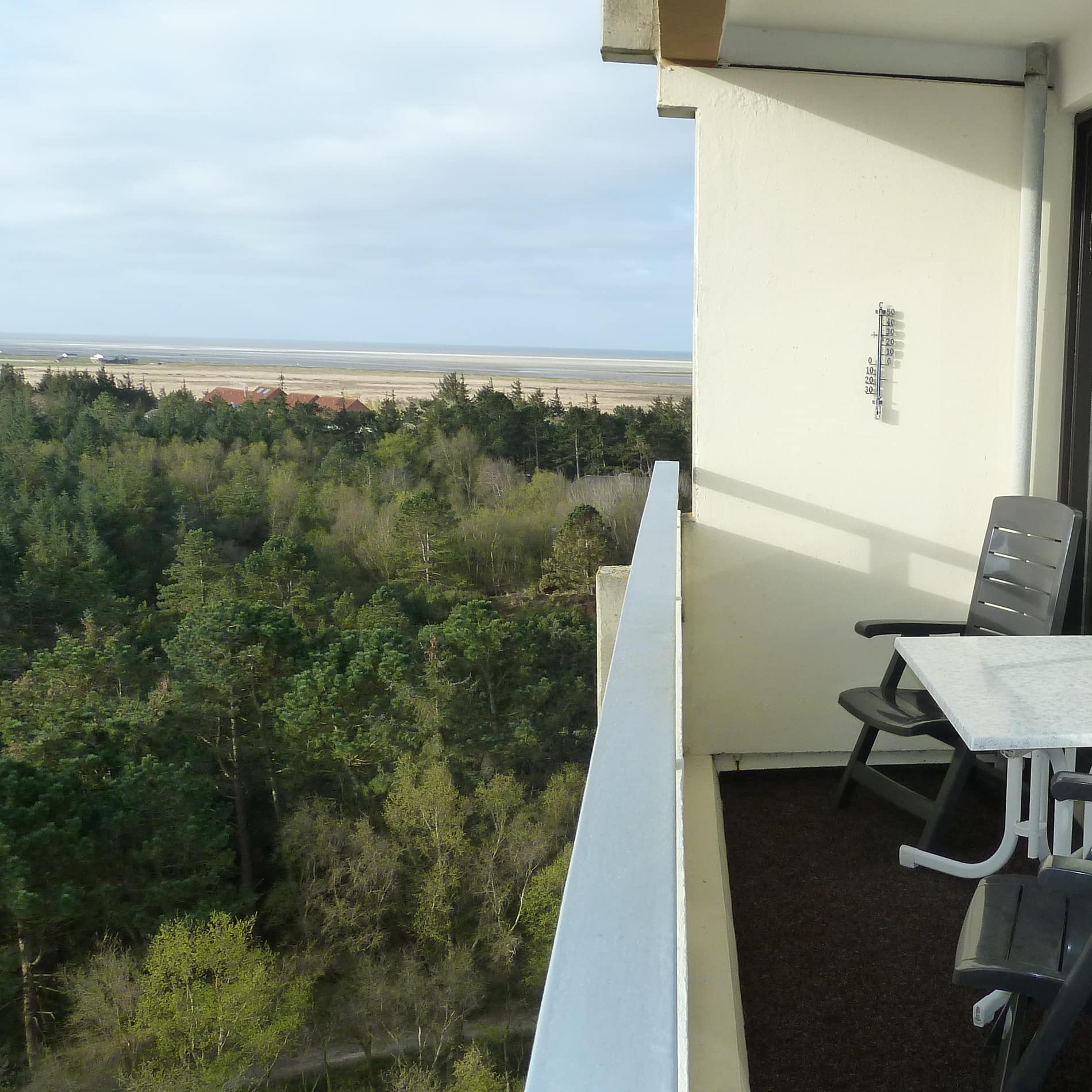 Balkon eines Ferienhauses in Sankt Peter-Ording mit Meerblick: jenseits eines Kiefernwäldchens der Sandstrand und die Nordsee