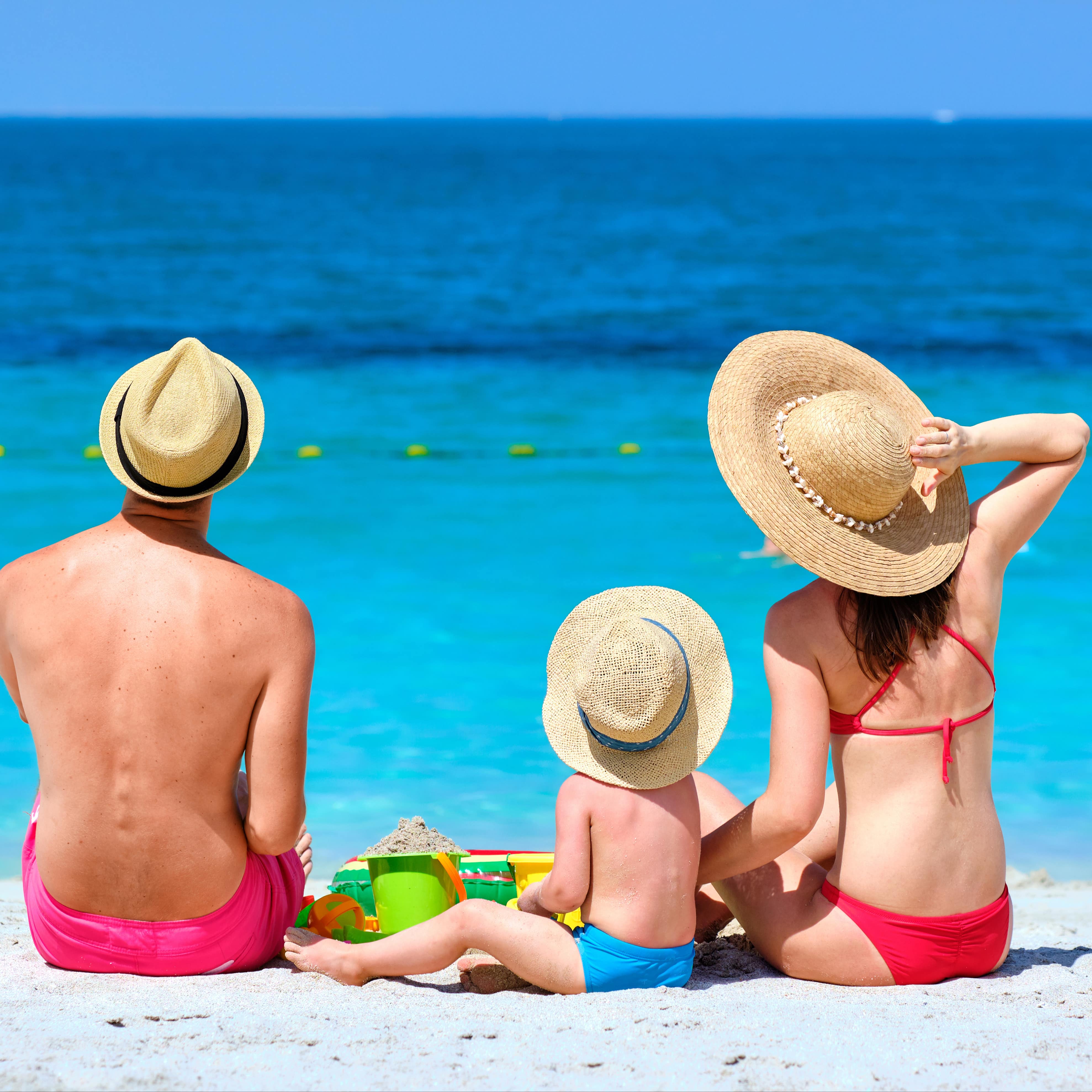 Rückenansicht: Eltern mit Kleinkind am Strand schauen aufs Wasser.