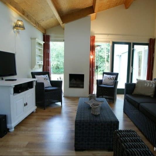 Ferienwohnung auf Texel mit großem Wohnraum mit Korbgarnitur, Fernseher und Esstisch sowie Blick auf eine Terrasse