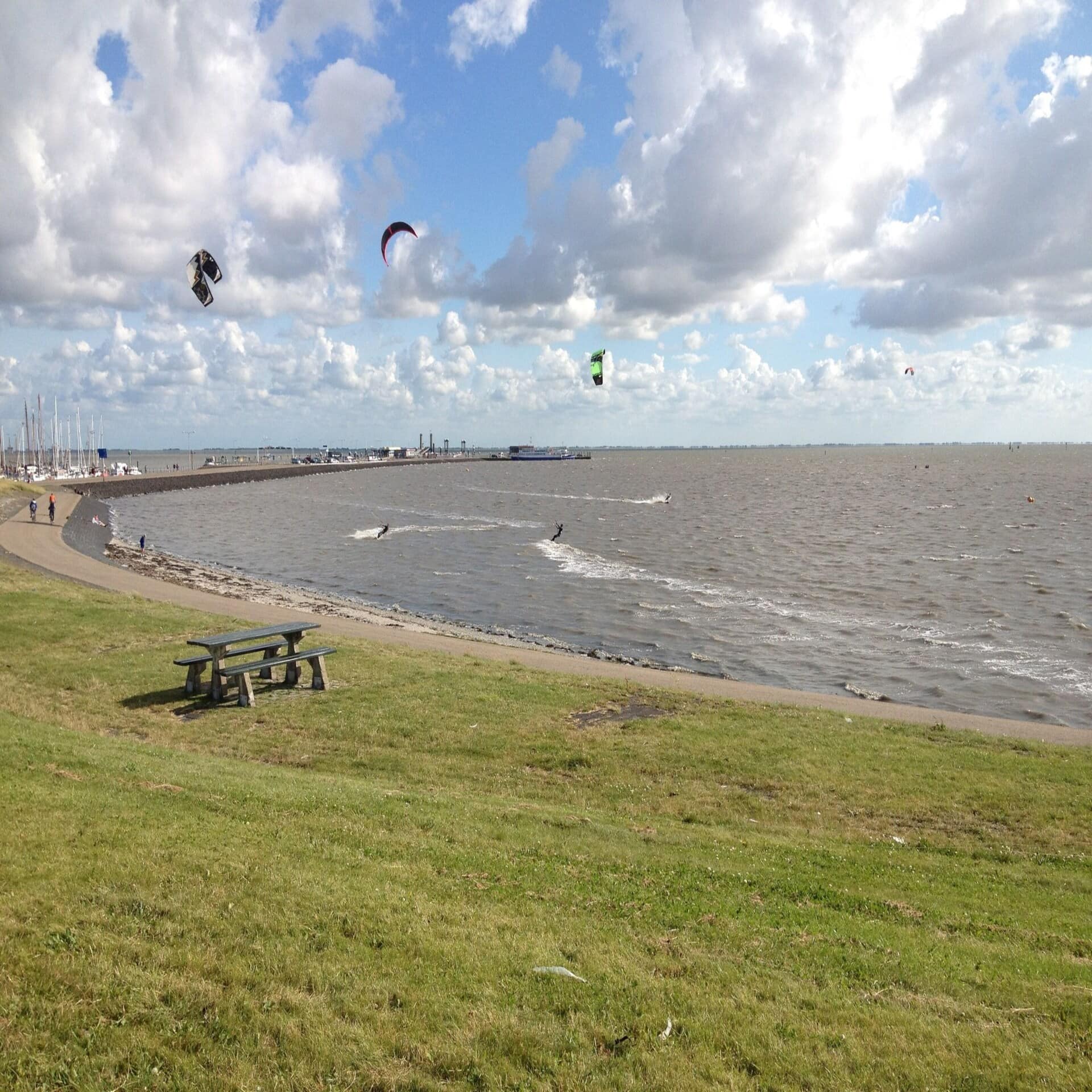 Kitesufer sausen neben dem Fähranleger durch das Meer. 