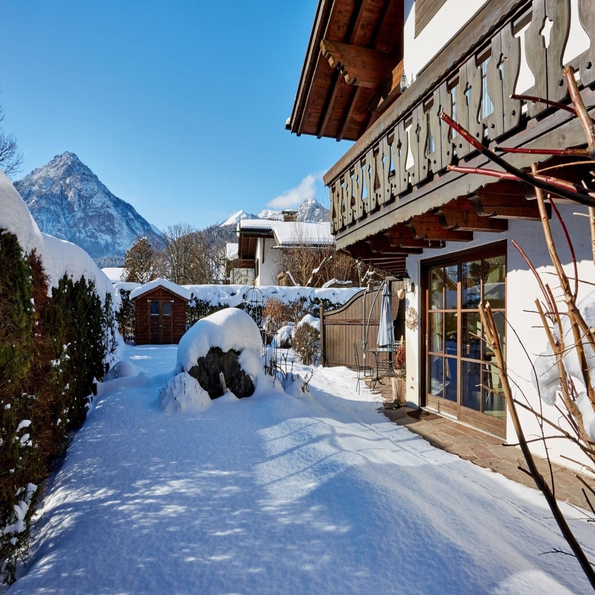 Haus mit verschneitem Garten und Blick auf die Zugspitze bei Sonnenschein.