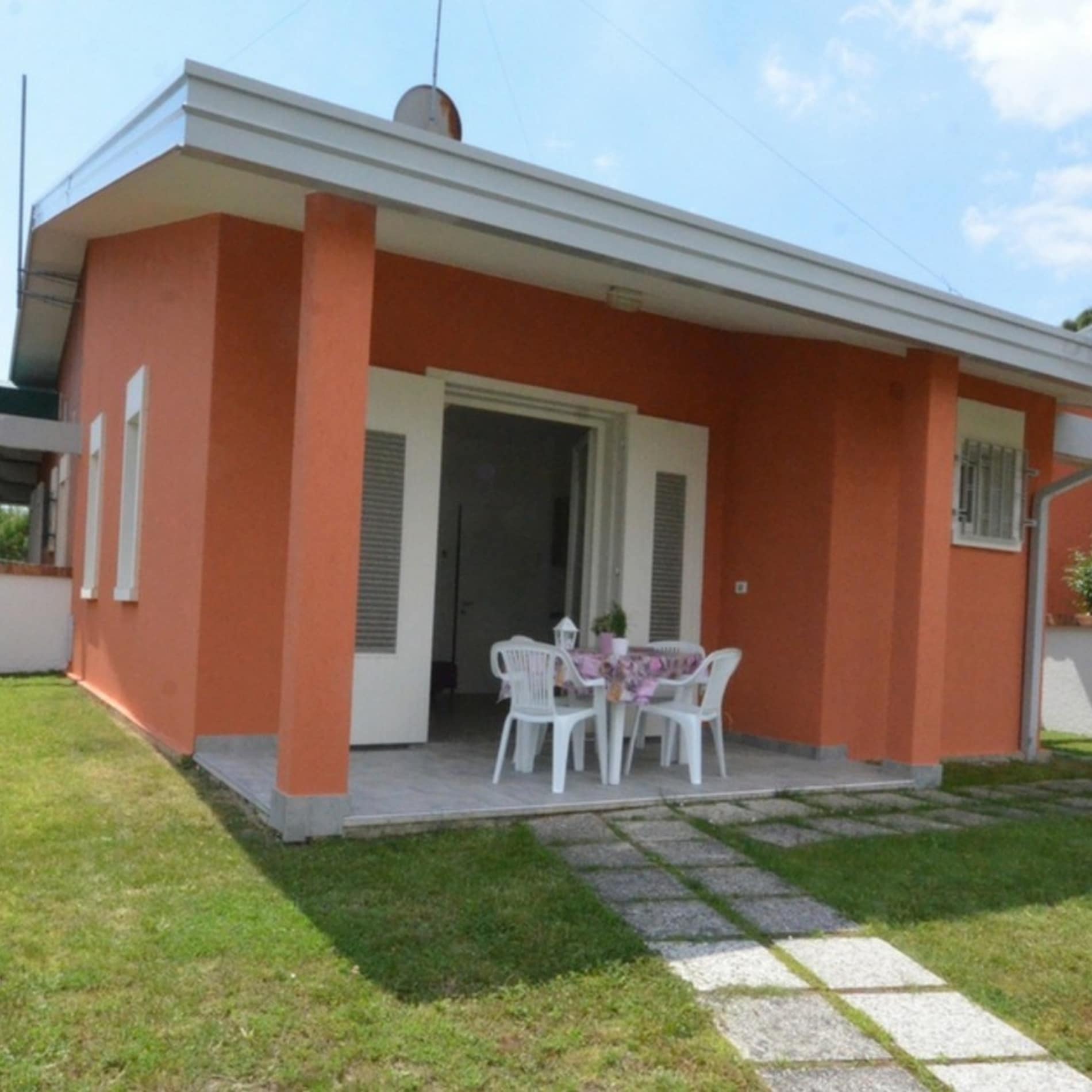 In rötlichen Tönen gestrichenes Ferienhaus in Bibione Pineda mit Tisch und Stühlen auf der Veranda