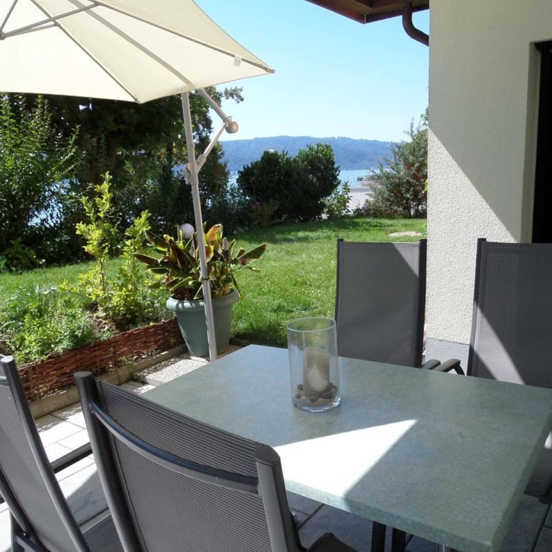 Terrasse und Garten einer Ferienwohnung in Konstanz mit Blick auf den Bodensee, durch die Büsche ist der See zu sehen.
