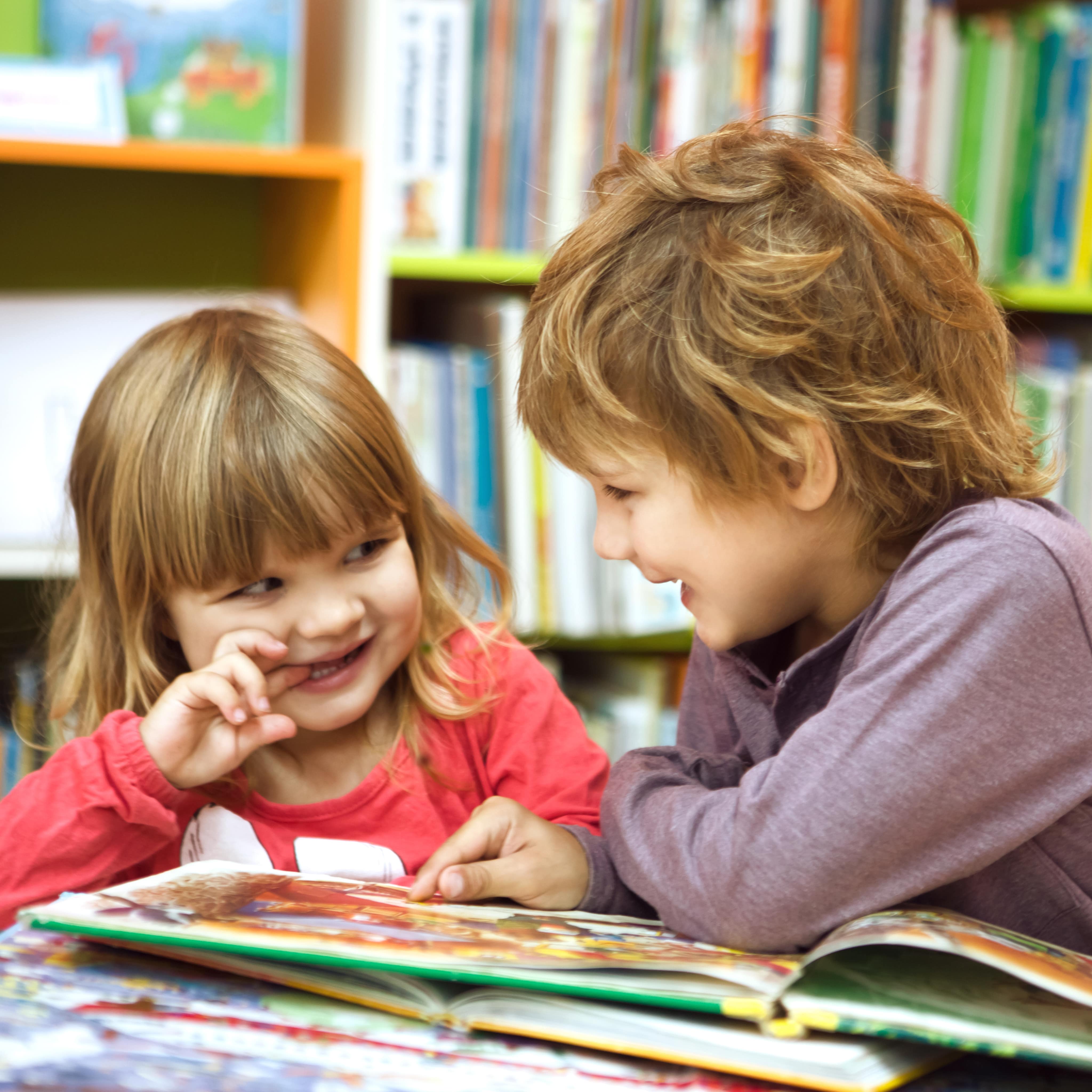 2 kleine Kinder in einer Bücherei schauen sich zusammen ein Buch an.