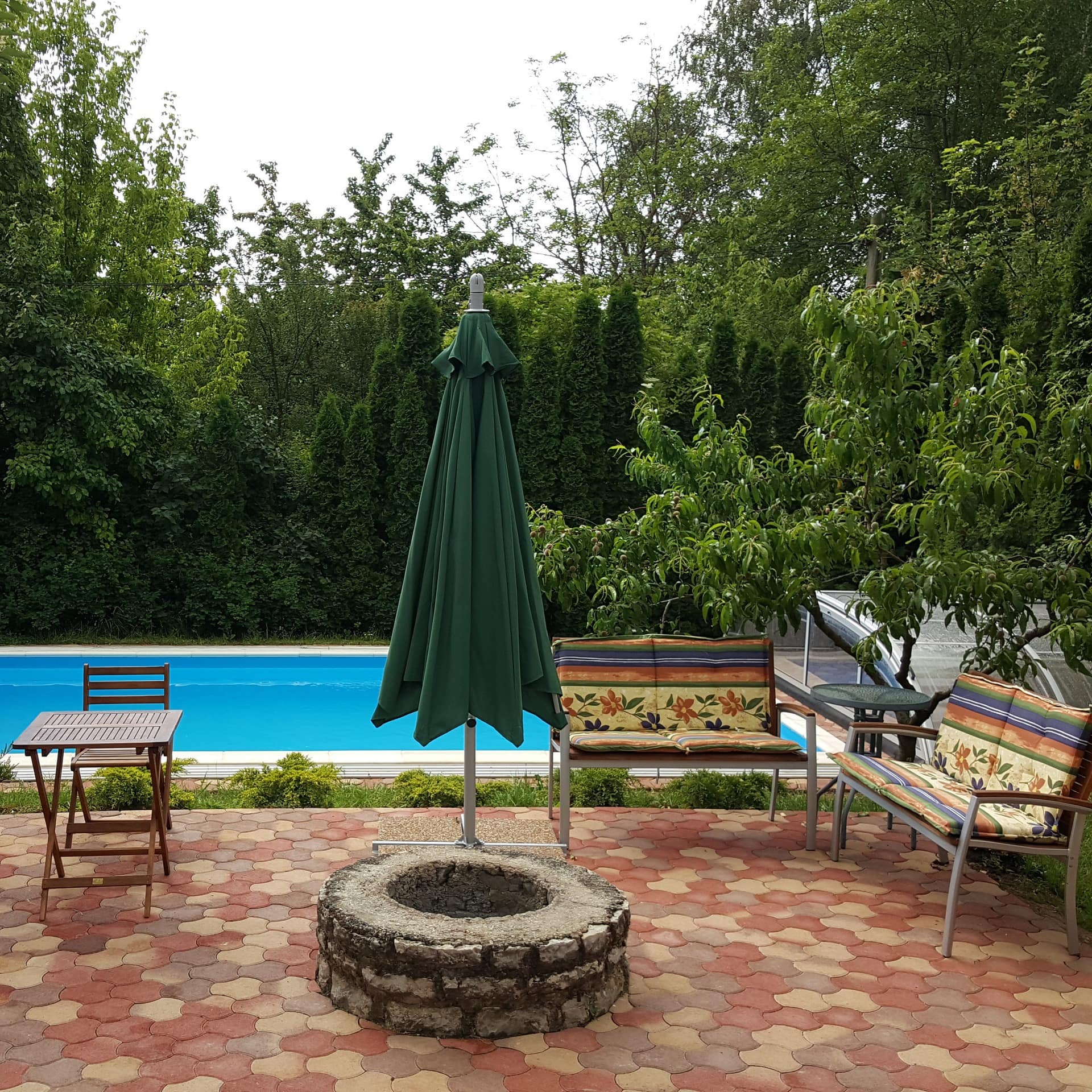 Blick von der Terrasse eines Ferienhauses am Balaton auf den Pool, auf der Terrasse sind Sitzgelegenheiten und Sonnenschirm