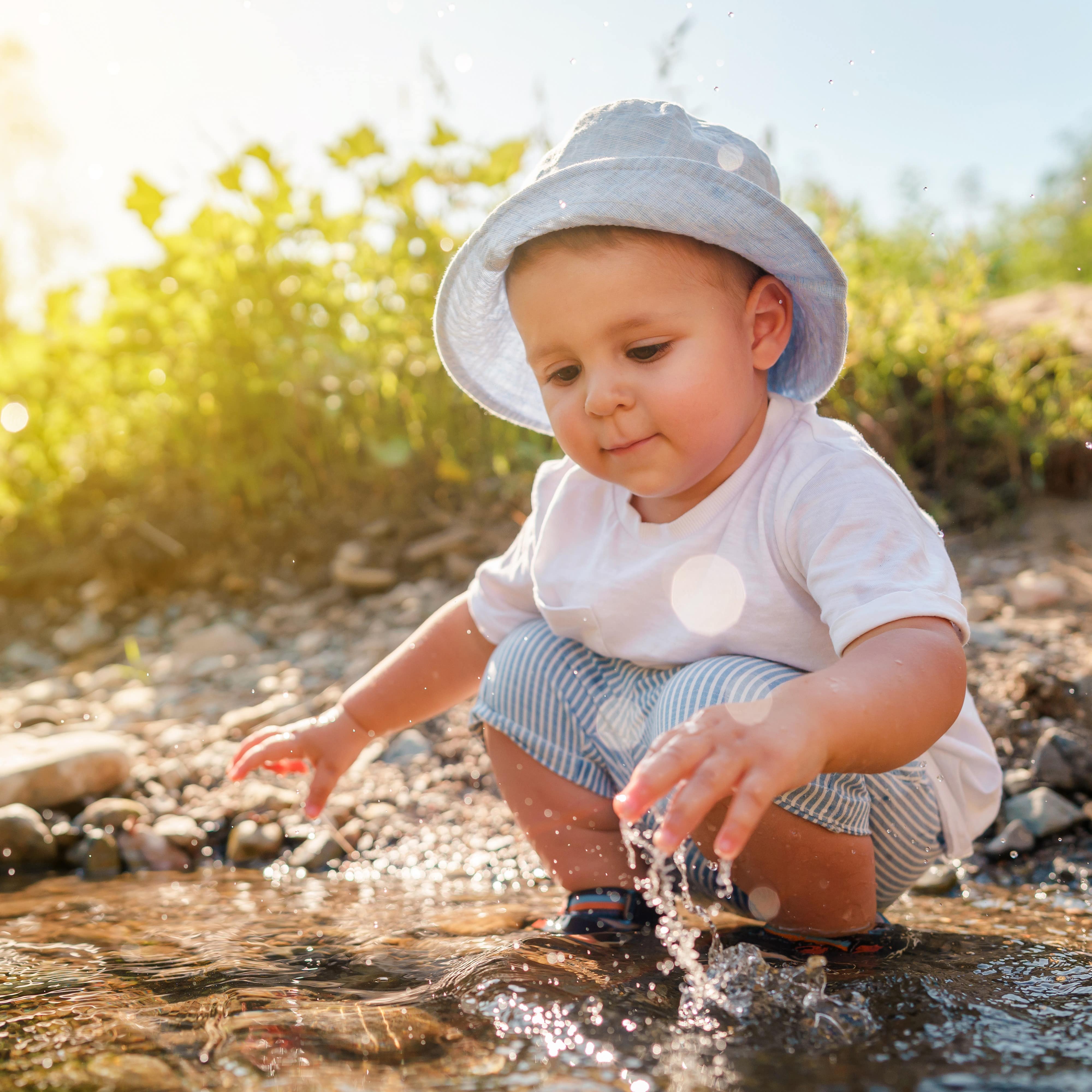 Ein Kleinkind in Sommerkleidung spielt im flachen Wasser eines Sees.