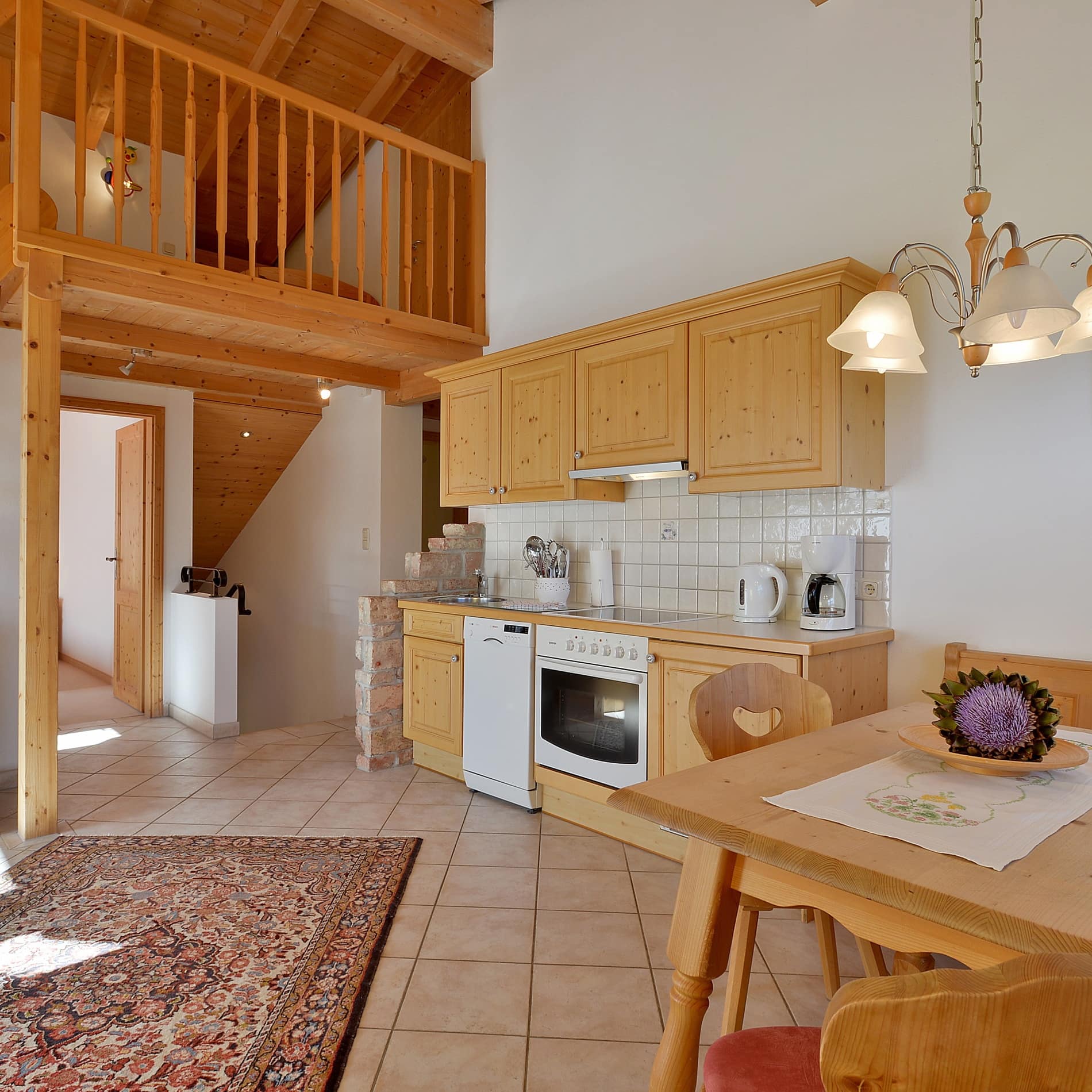 Geräumige Wohnküche mit Mobiliar aus hellem Holz und Treppe ins obere Geschoss der Ferienwohnung 