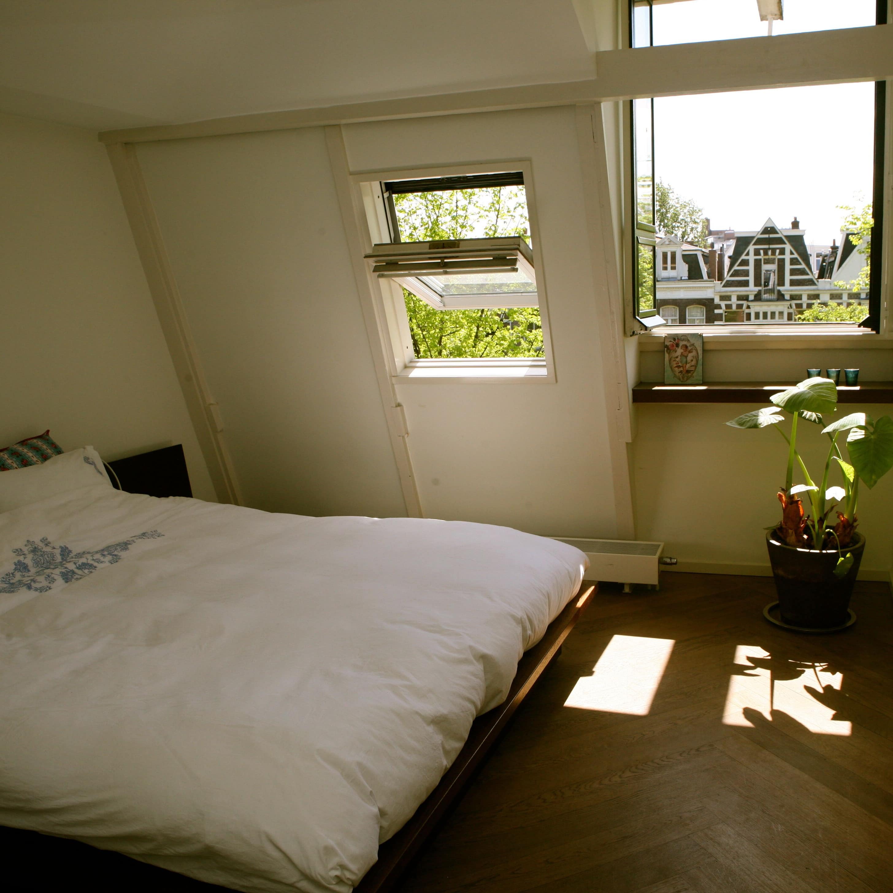 Ferienwohnung in Zandvoort – gemütliches Schlafzimmer unter der Dachschräge mit Pflanze und Blick auf typisch niederländische Giebel