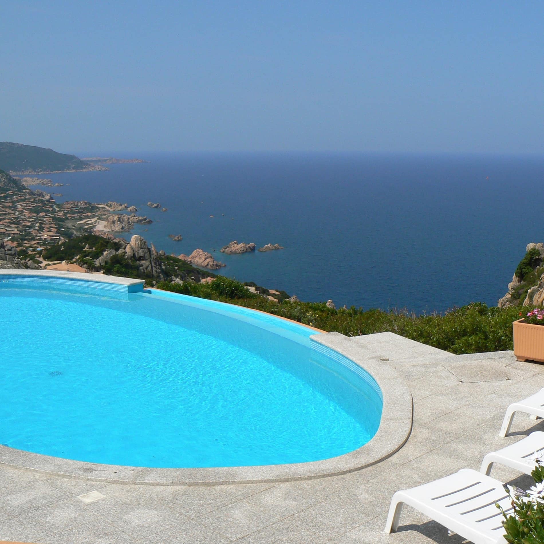 Über dem hellblauen Oval der Pools, der zur Ferienwohnung in Sardinien gehört, schweift der Blick über das tiefblaue Meer zum Horizont