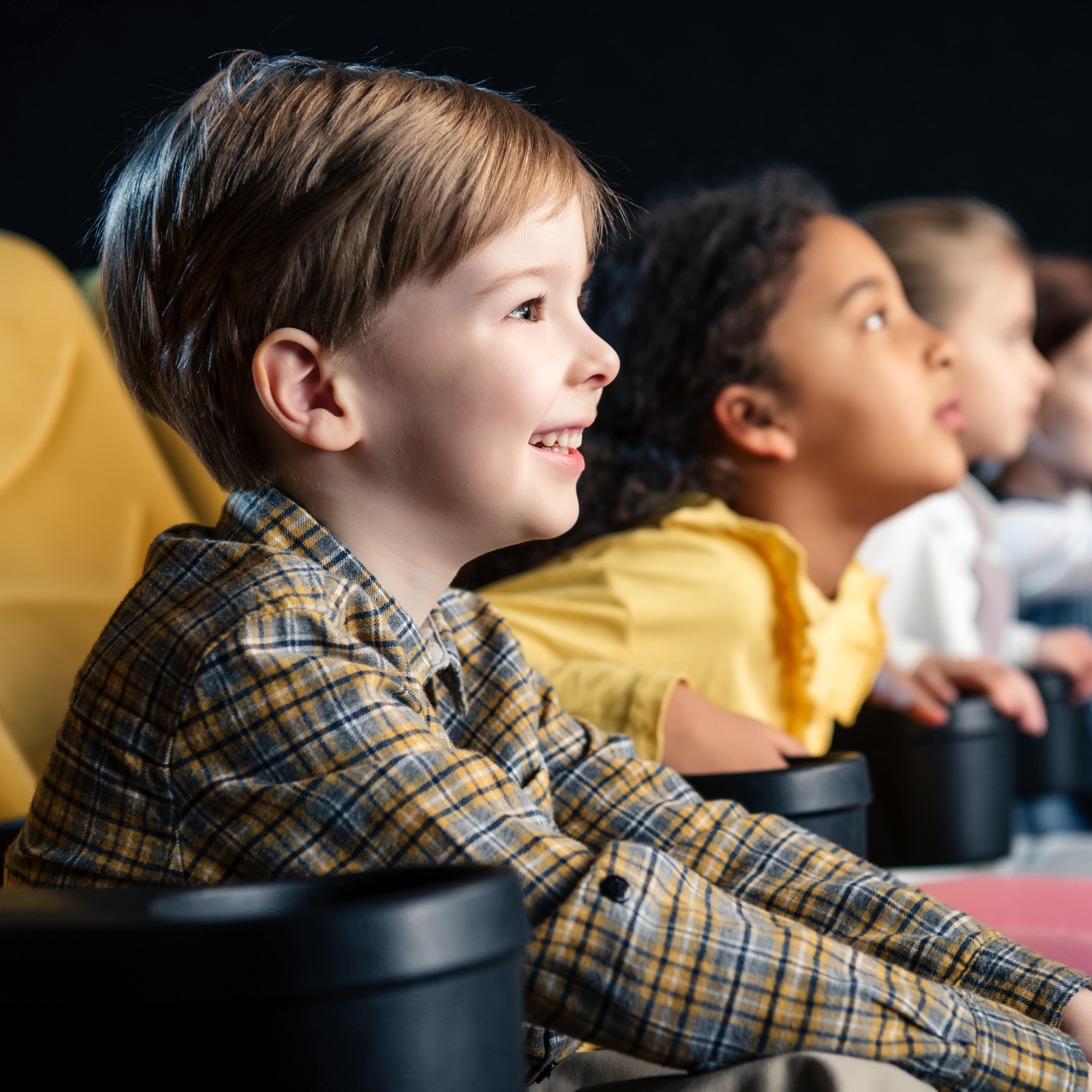 Blick von der Seite auf Kinder die nebeneinander in gelben Sitzen im Kino sitzen.