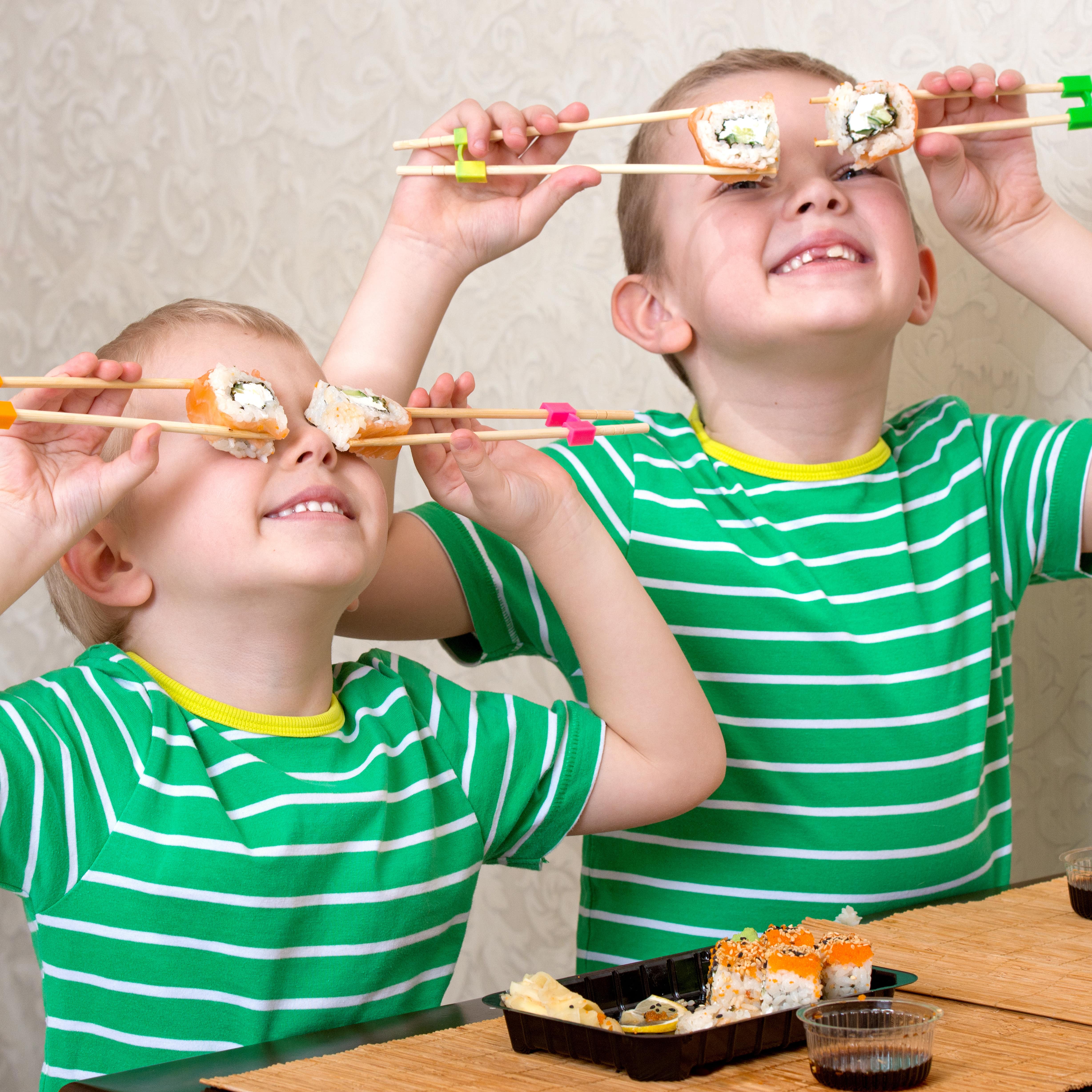 2 Jungen in grün-weiß gestreiften T-Shirts Essen Sushi und halten sich mit Stäbchen je 1 Sushi-Stück vor jedes Auge. 