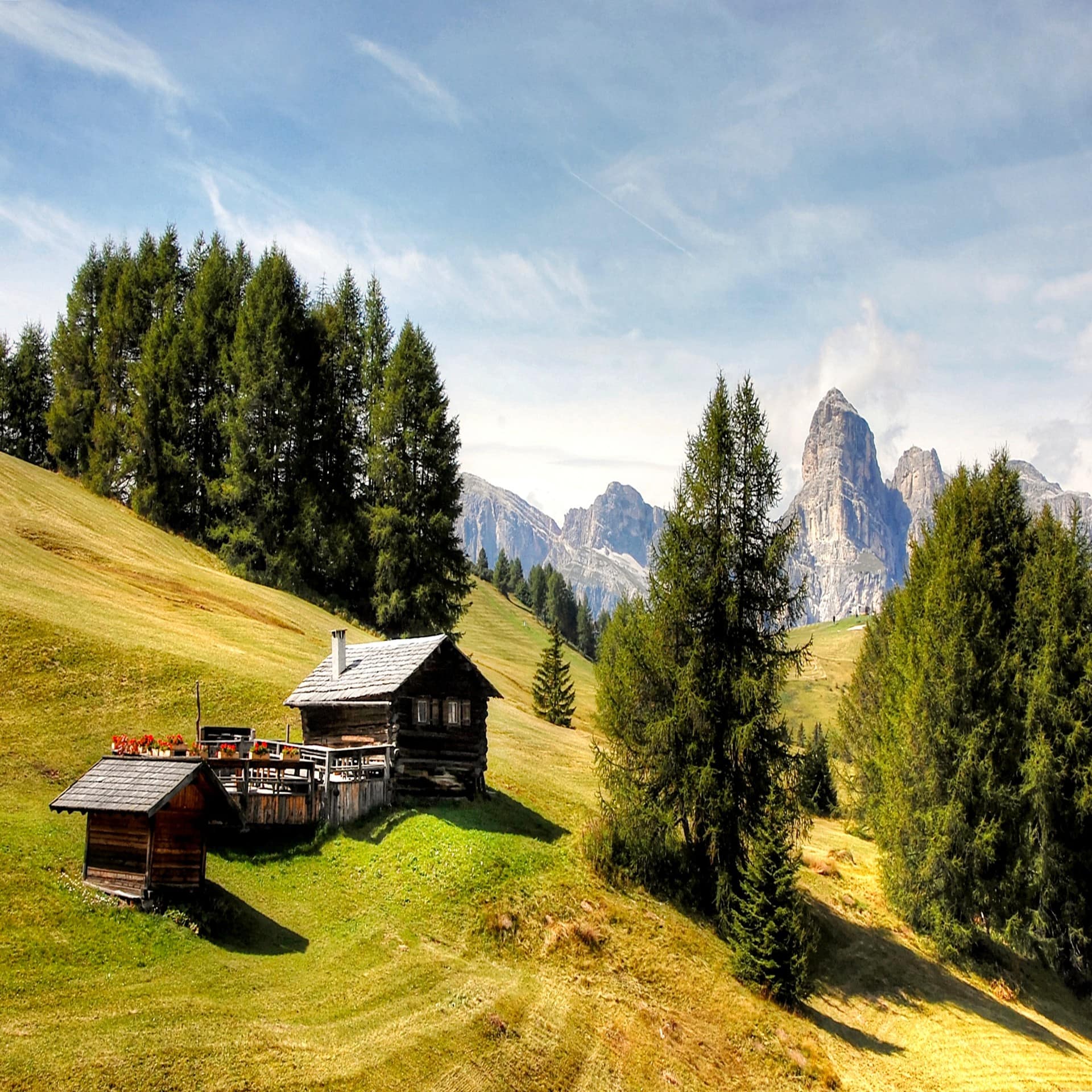 Blockhaus auf einer sommerlichen Almwiese in Gröden, die Berge im Hintergrund. 