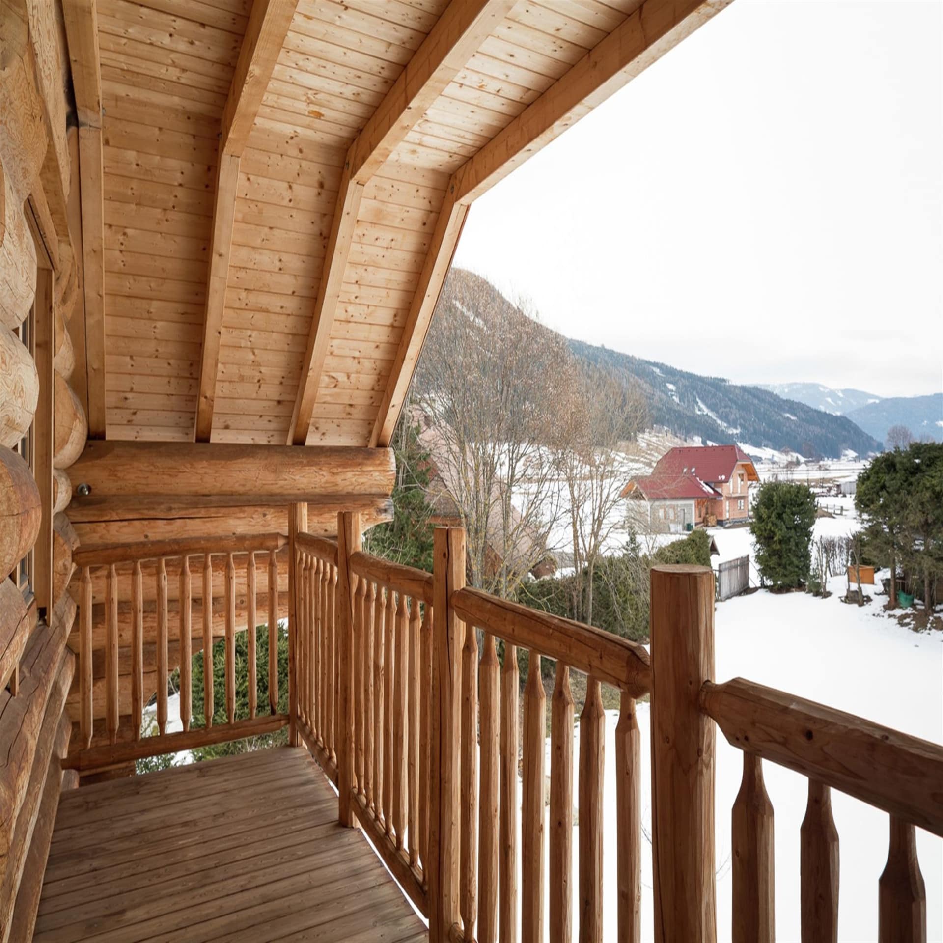 Holzbalkon eines Holzhauses mit Blick auf den verschneiten Ort Obertauern.