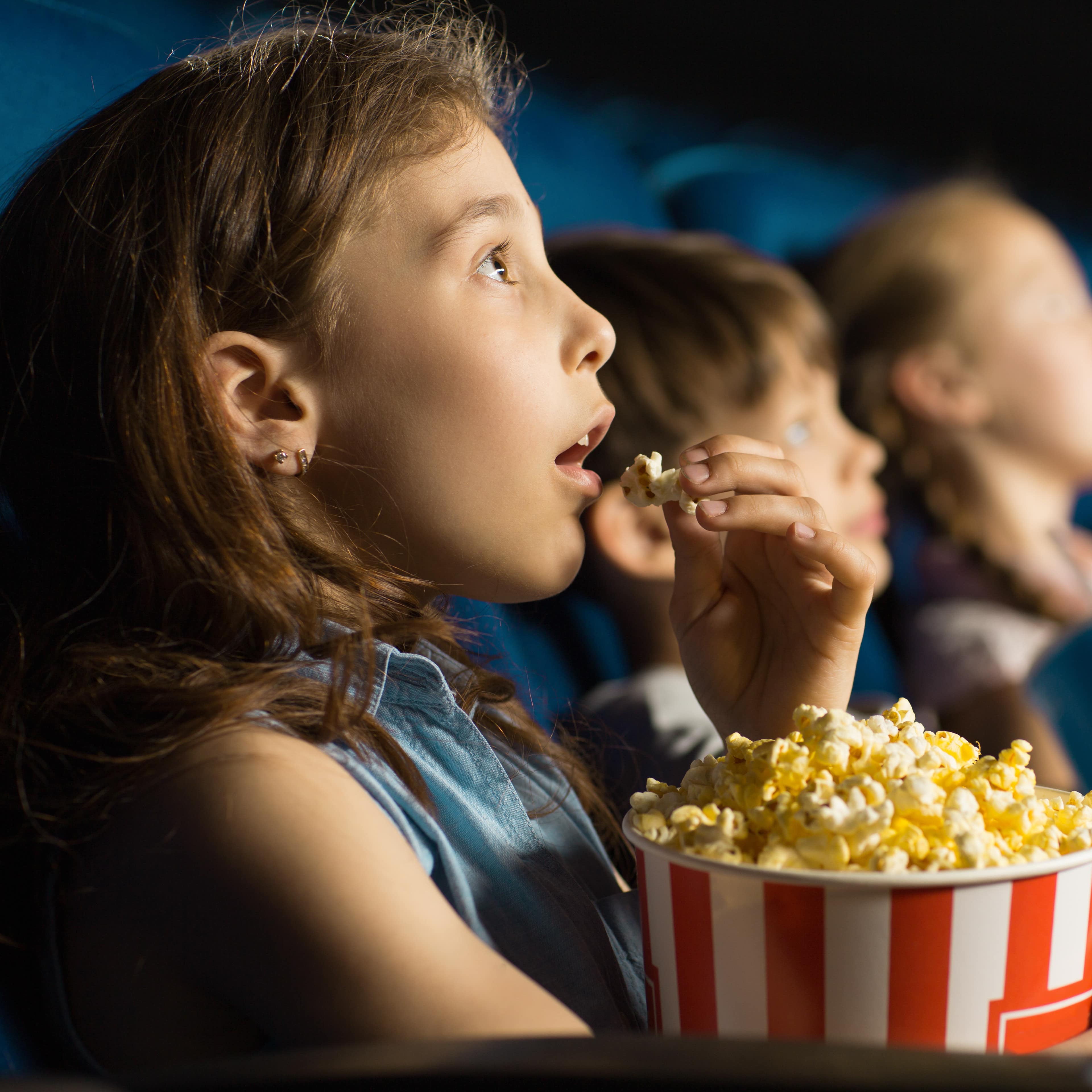 Nahaufnahme: Ein Mädchen in Sommerkleidung in einem Kinositz schaut einen Film und isst Popkorn.