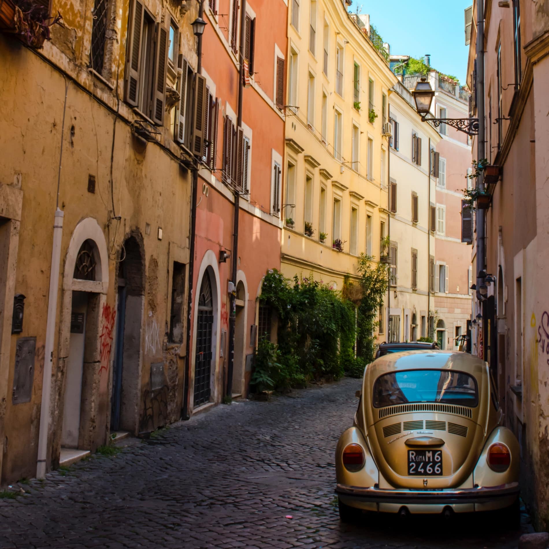 Ein VW-Käfer mit römischem Nummernschild steht in einer kopfsteingepflasterten Gasse des Quartiers Trastevere