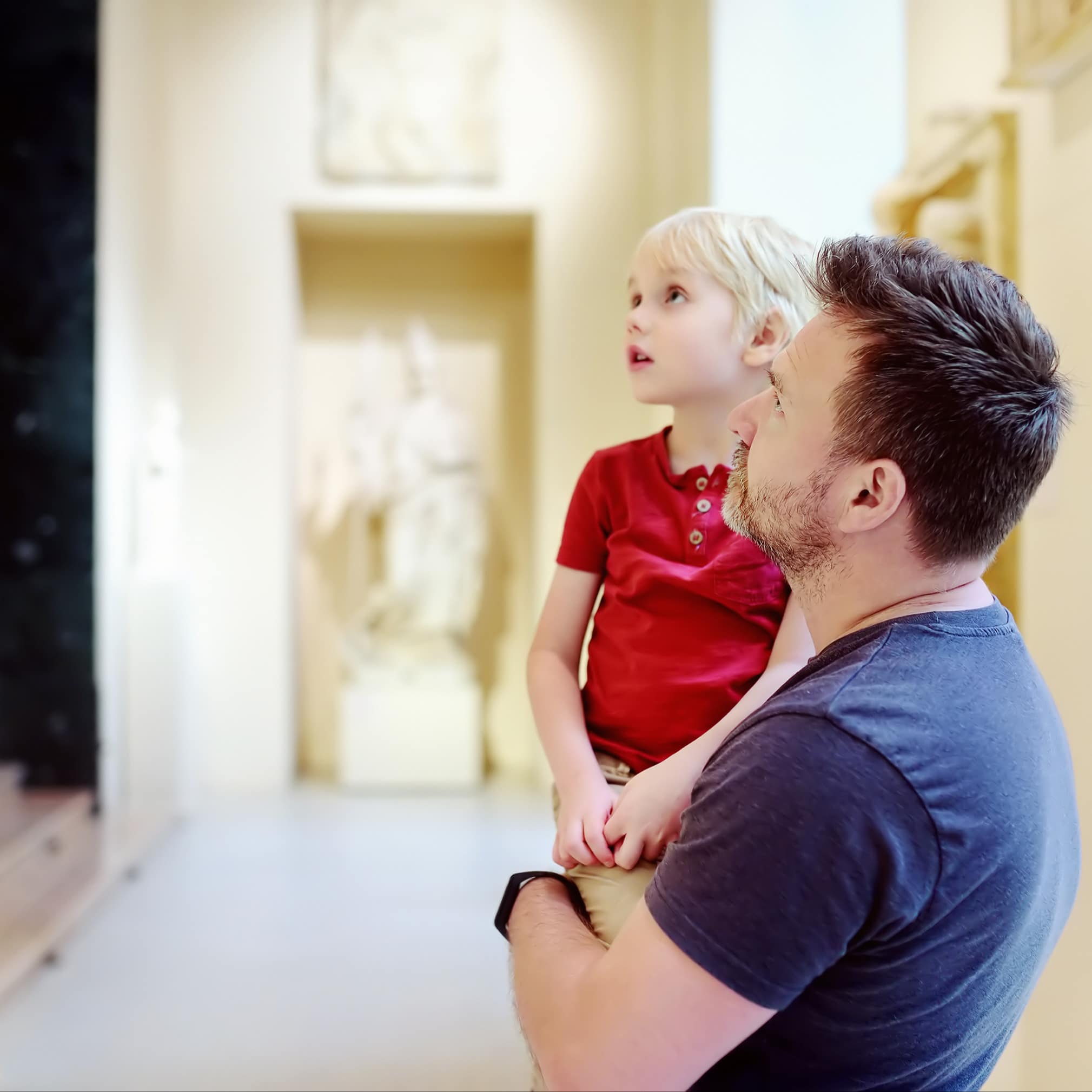 Vater trägt seinen Sohn auf dem Arm, beide schauen Statuen in einem Museum an.  Image URL: 