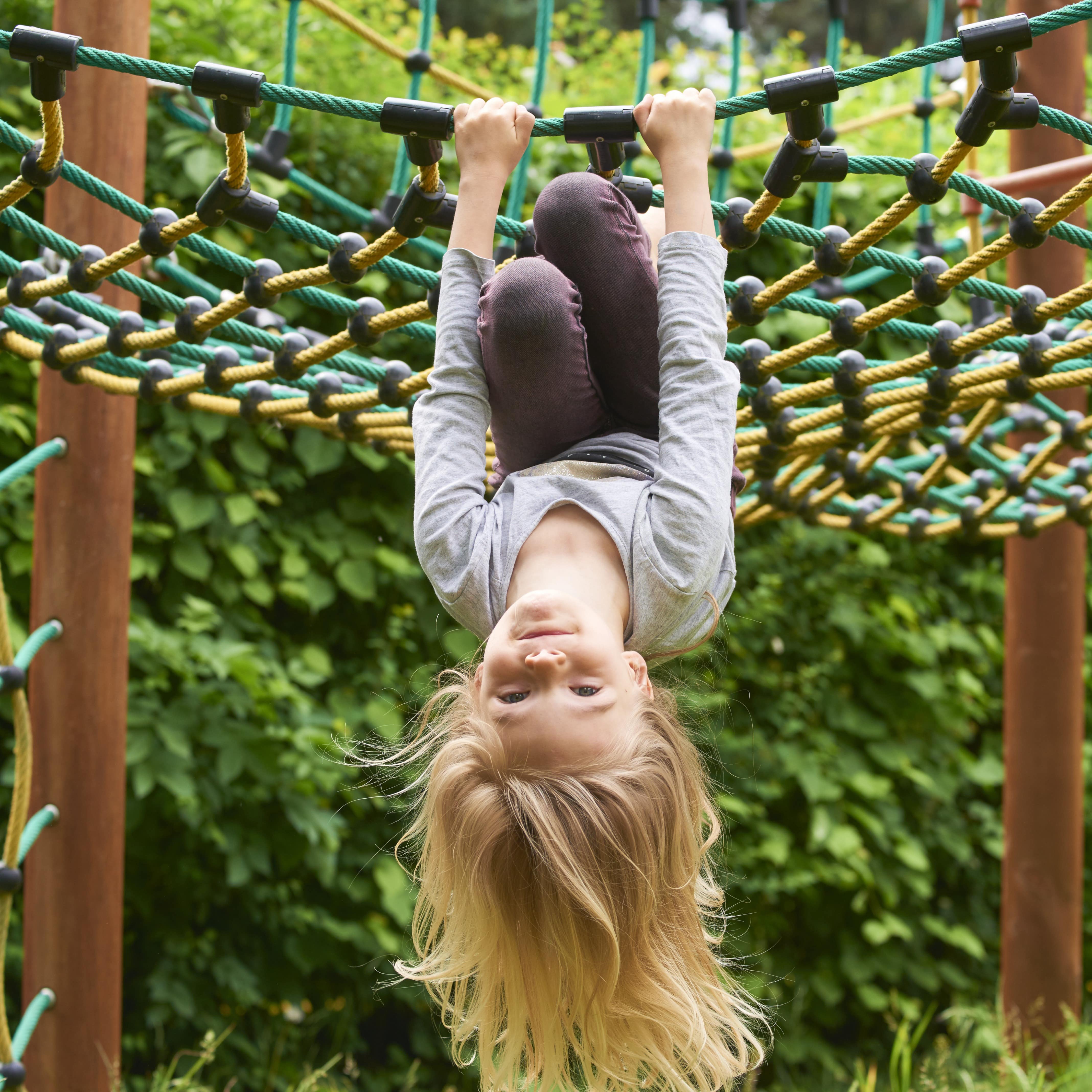 Mädchen mit langen blonden Haaren hängt kopfüber in einem Kletternetz.