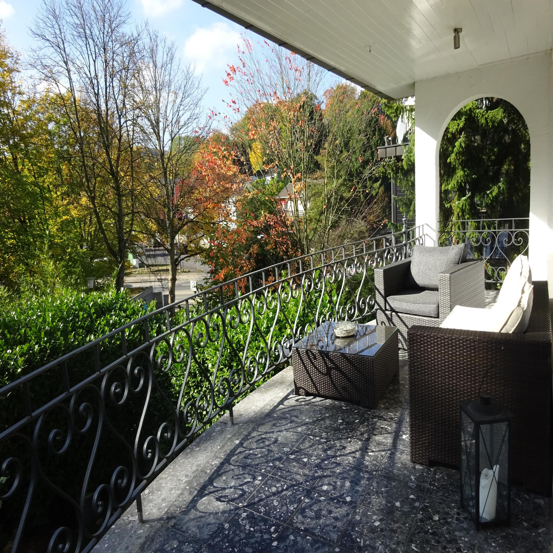 Großer Balkon mit Sitzgruppe und Blick auf herbstliche Bäume. 