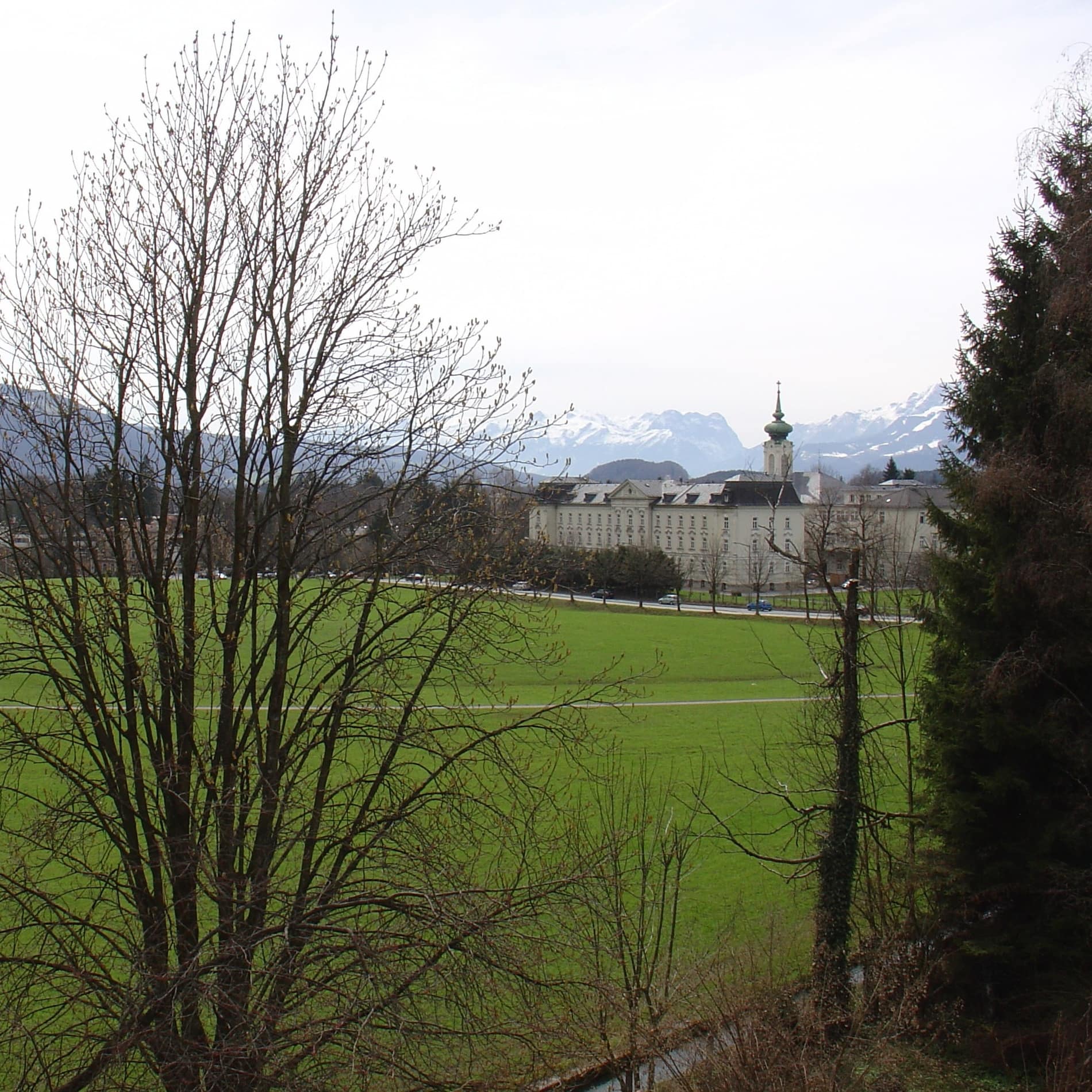 Von der Terrasse der Ferienwohnung auf dem Land sind jenseits einer Wiese historische Bauten und die schneebedeckten Berge sichtbar