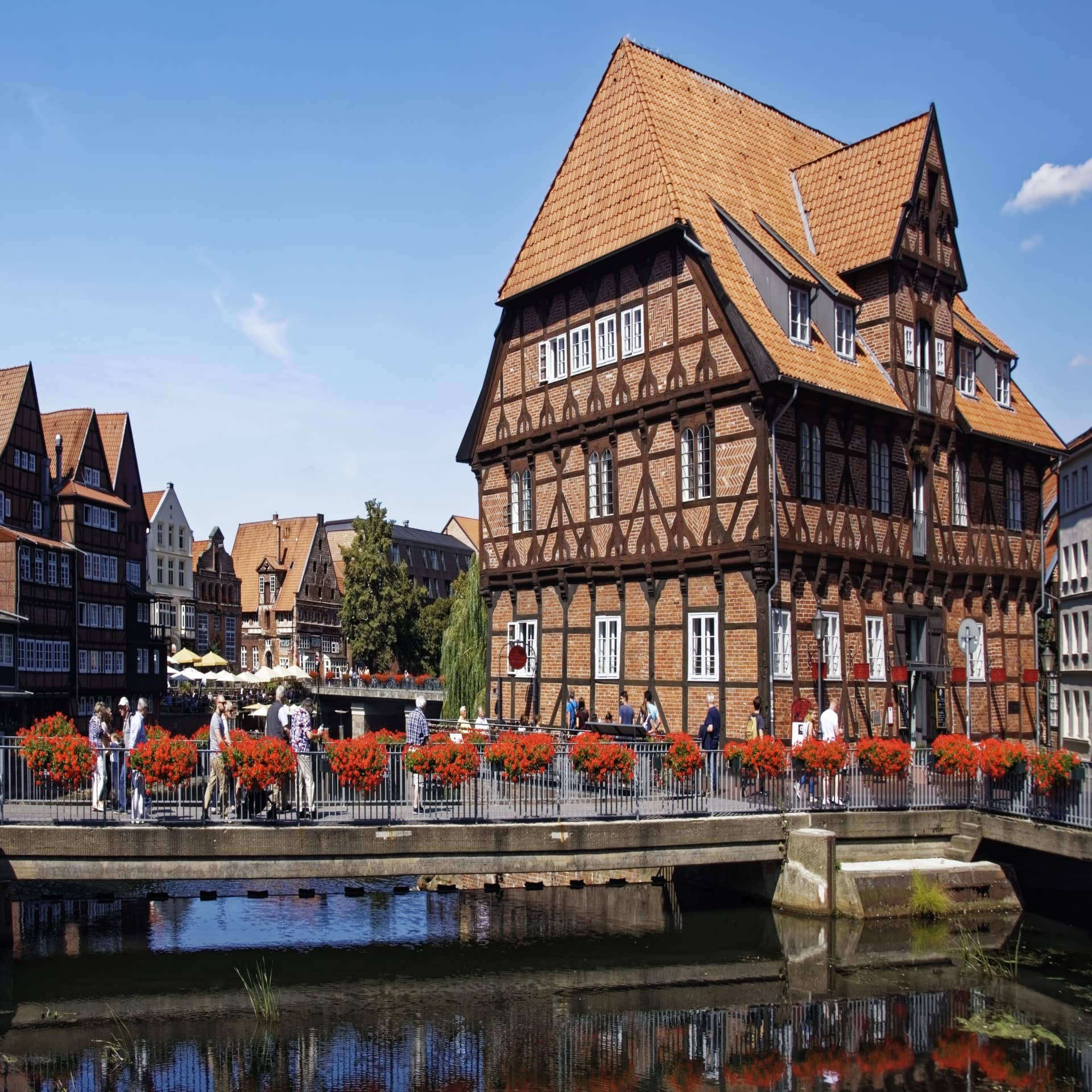 Blick auf eine mit roten Blumen geschmückte Brücke und ein rotes Fachwerkhaus in der Lübecker Altstadt.