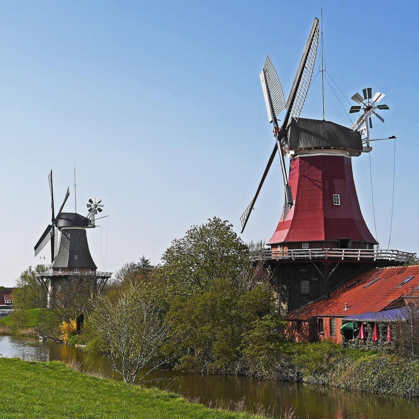 Windmühlen und Häuser an einem Fließgewässer in Greetsiel
