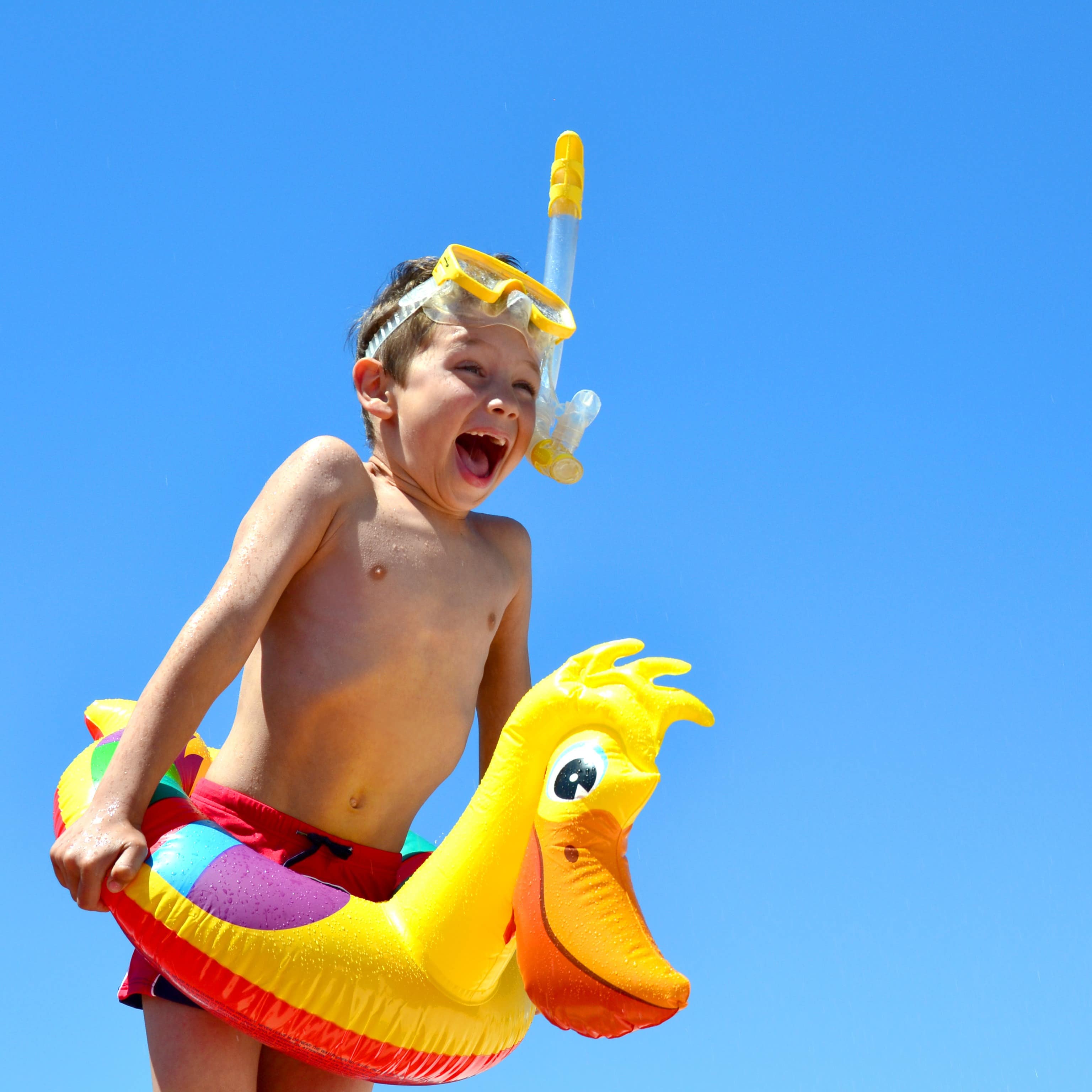 Junge mit Enten-Schwimmring, Taucherbrille und Schnorchel vor blauem Himmel