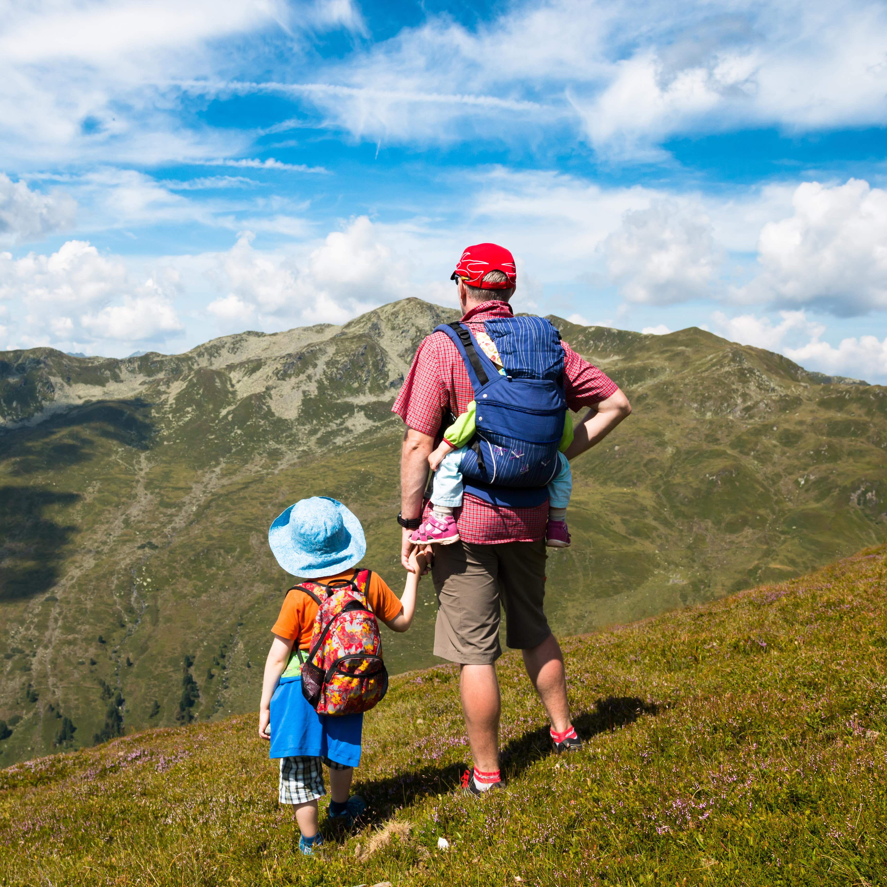 Vater mit Baby auf dem Rücken und Kleinkind an der Hand blickt auf das Bergland.