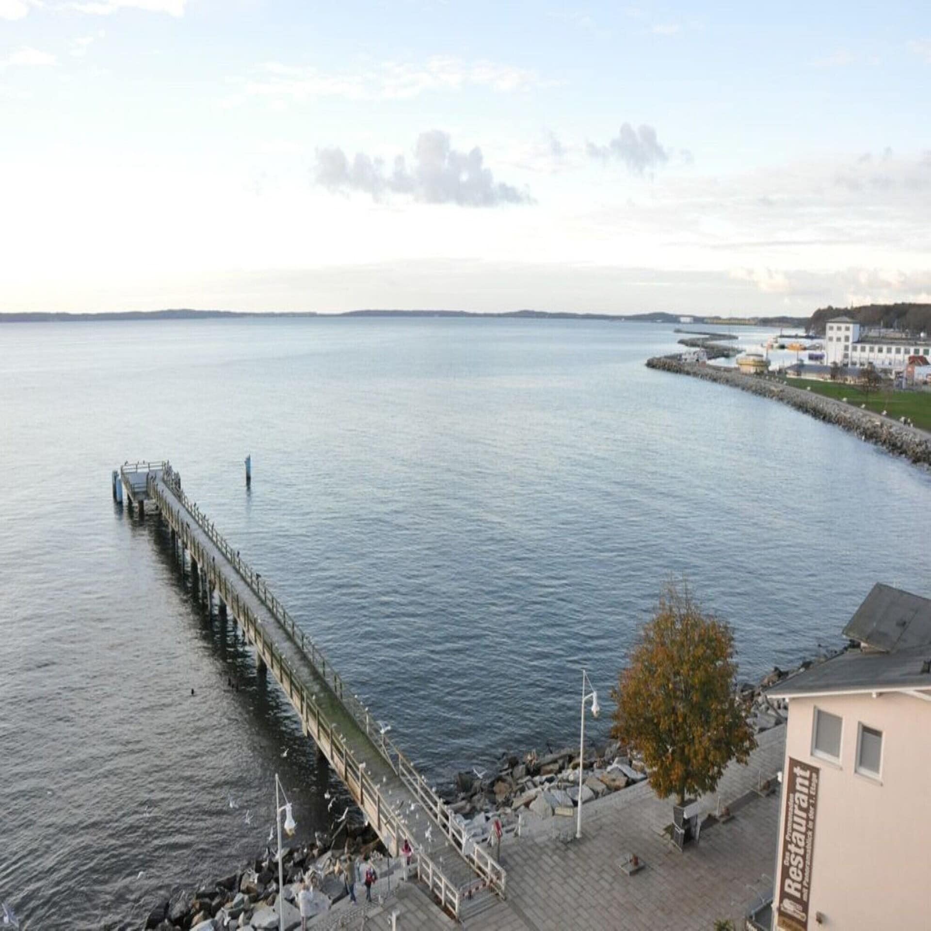 Blick von einem Balkon auf das Meer mit Seebrücke und die Promenade. 