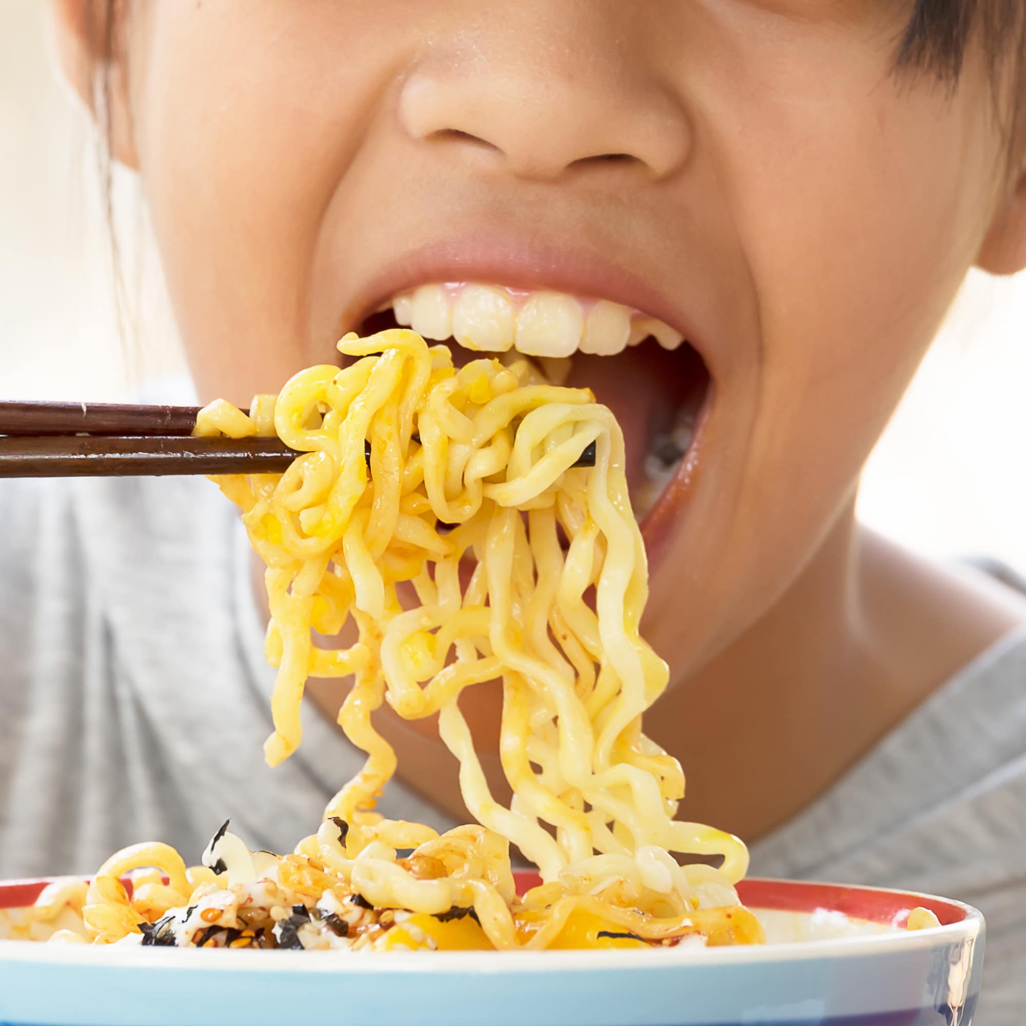 Nahaufnahme: Ein Kind isst chinesische Nudeln mit Stäbchen.