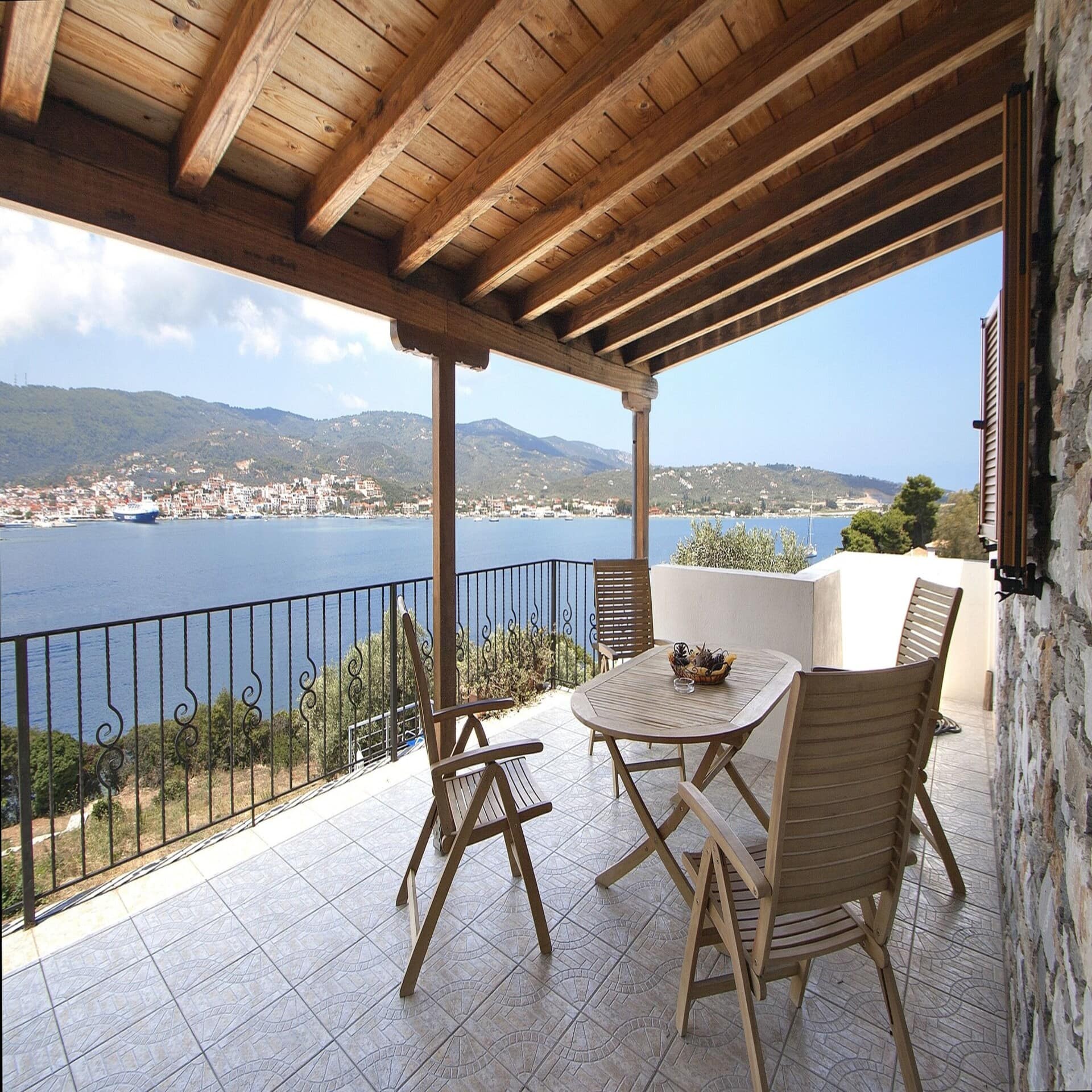 Große Terrasse mit Tisch und Stühlen und Blick auf das Meer. In der Ferne eine Stadt.