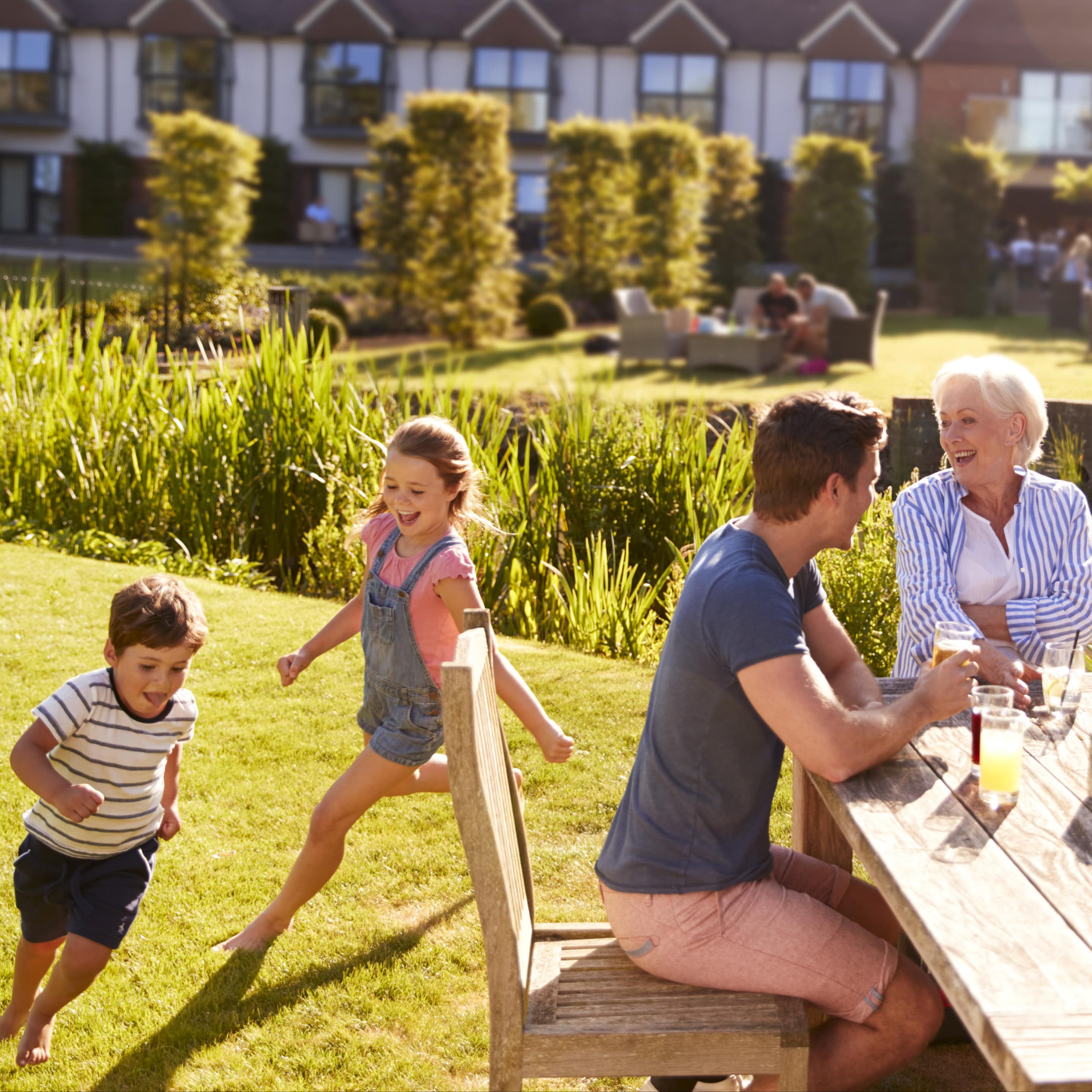 Im Restaurantgarten: Eltern und Großeltern sitzen am Tisch und trinken Bier und Wein, 2 Kinder rennen umher.