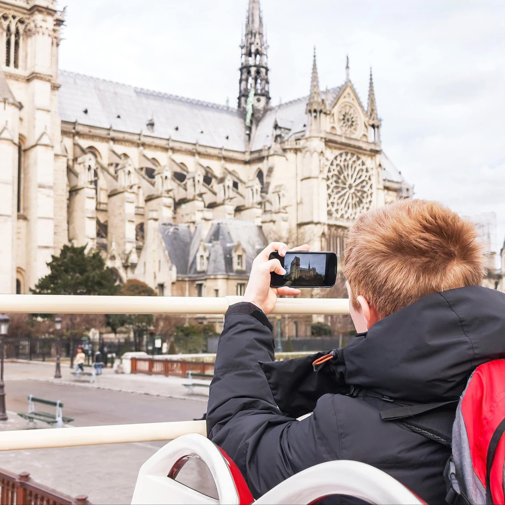 Ein Junge in einem offenen Sightseeingbus fotografiert Notre Dame.