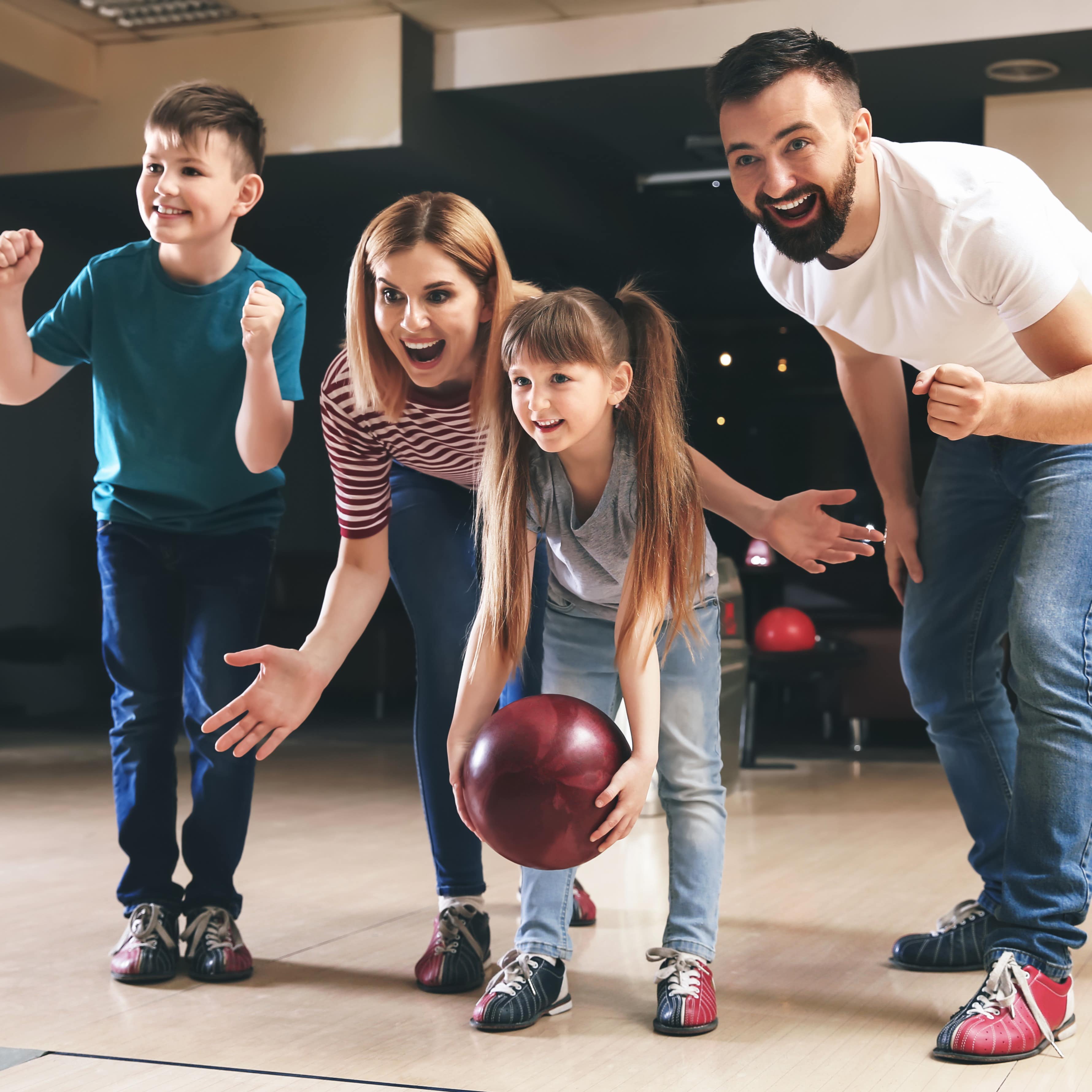 Eine Familie mit 2 Kindern beim Bowling, Mädchen mit Zöpfen halt eine Bowlingkugel in der Hand.