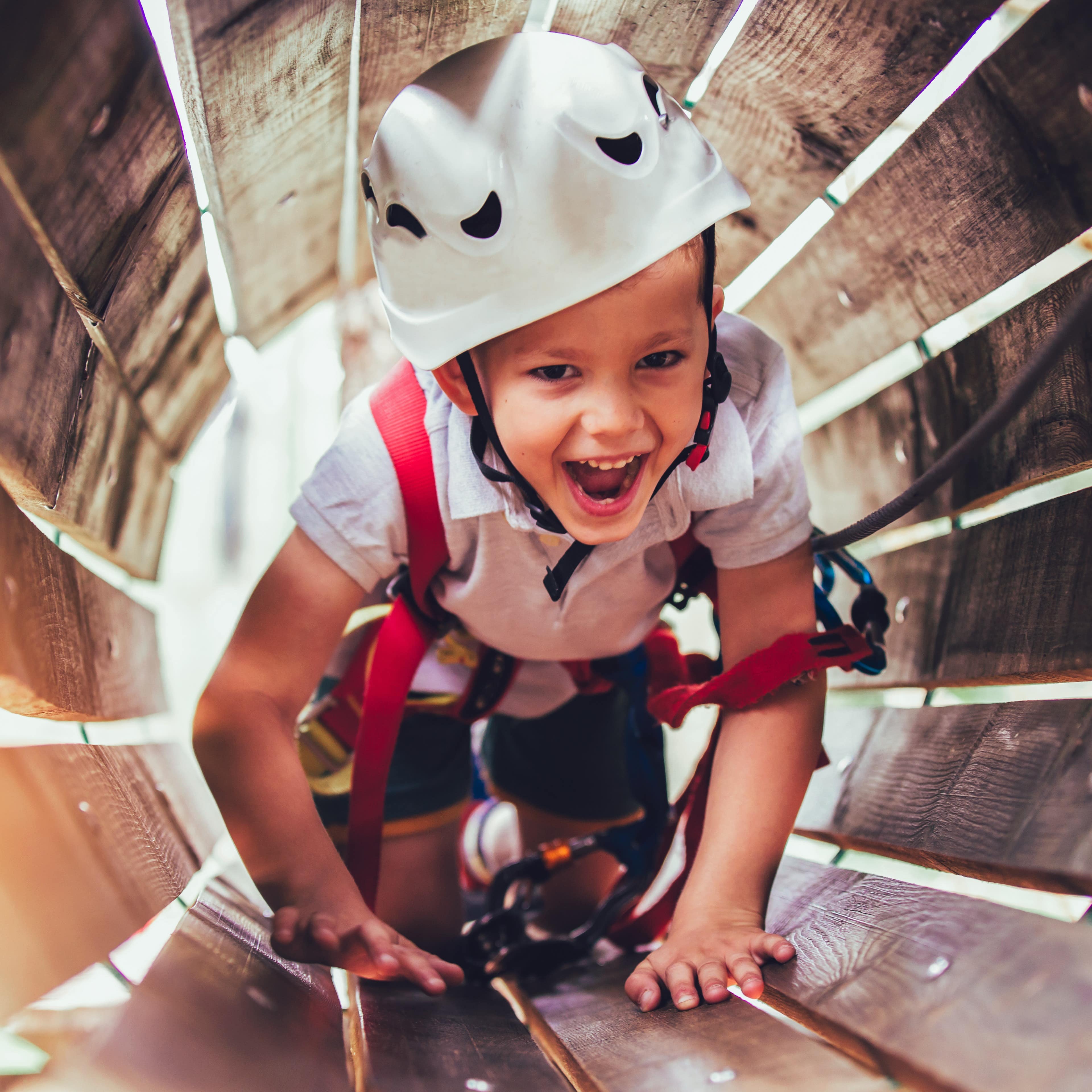 Ein Junge mit Kletterausrüstung und Helm krabbelt durch einen Holztunnel.