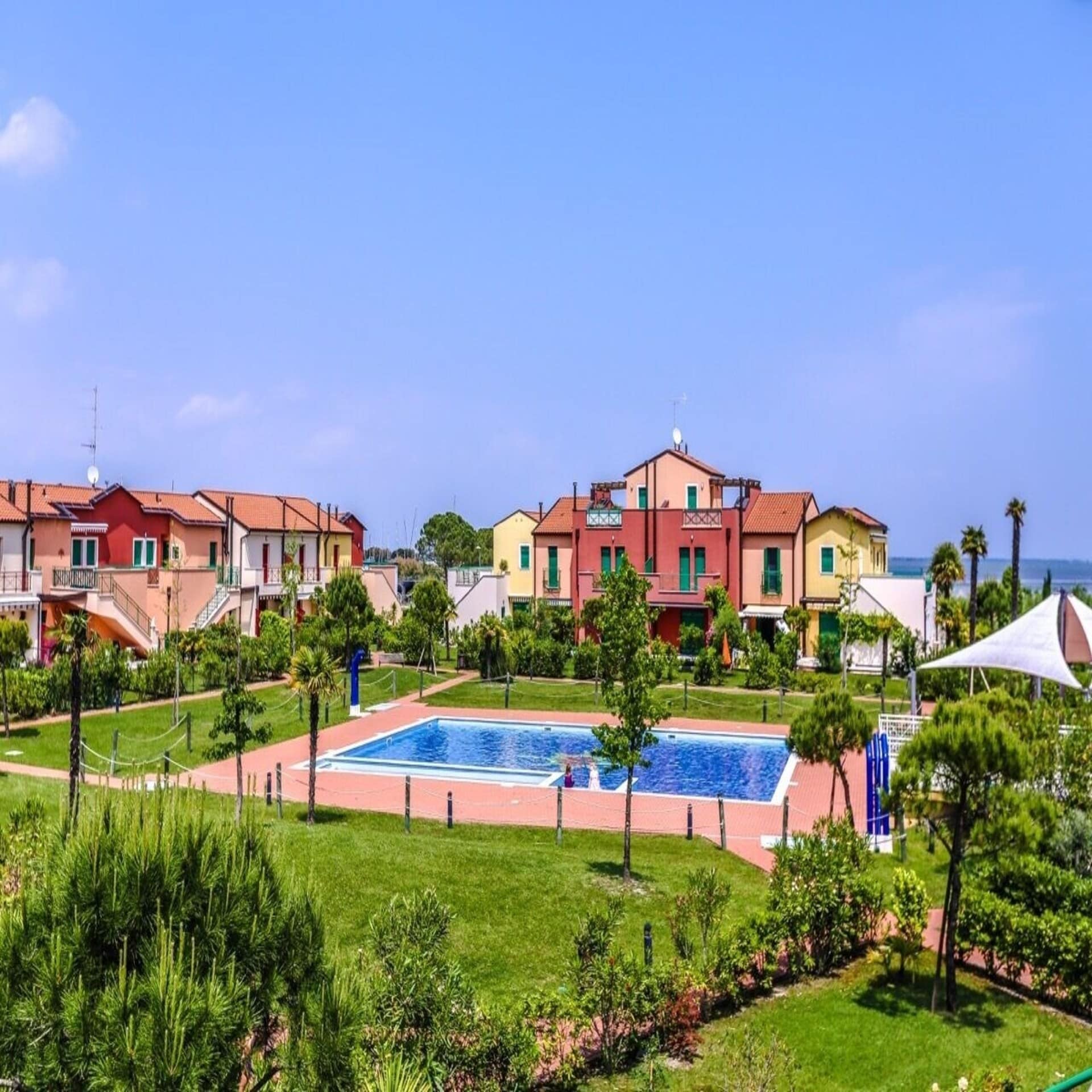 Ferienanlage mit bunten Häusern, Pool und gepflegtem Garten. Im Hintergrund das Meer.