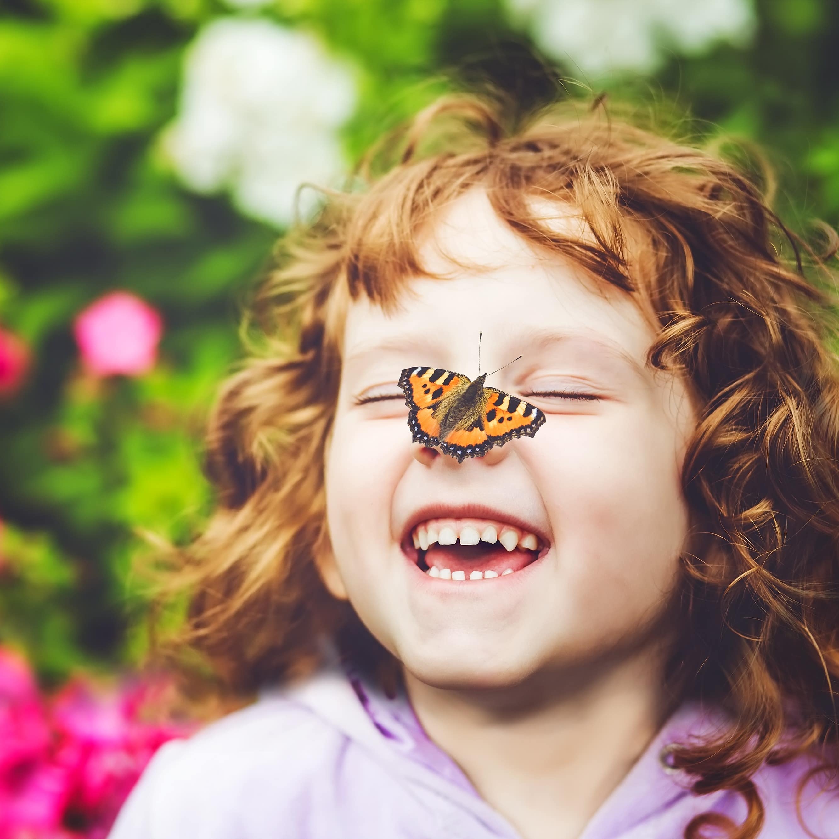 Schmetterling auf der Nase eines lachenden Mädchens mit roten Locken, sie hat die Augen geschlossen. 