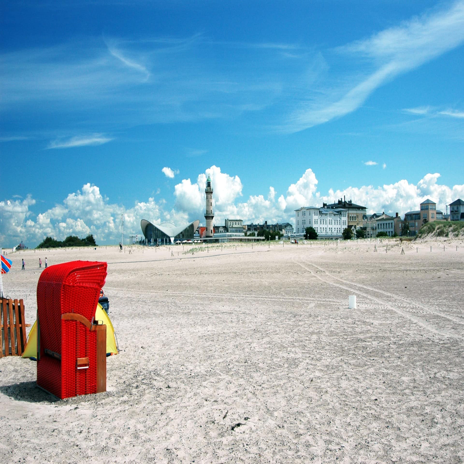 Roter Strandkorb mit Blick auf den weitläufigen Strand und Gebäude von Warnemünde.